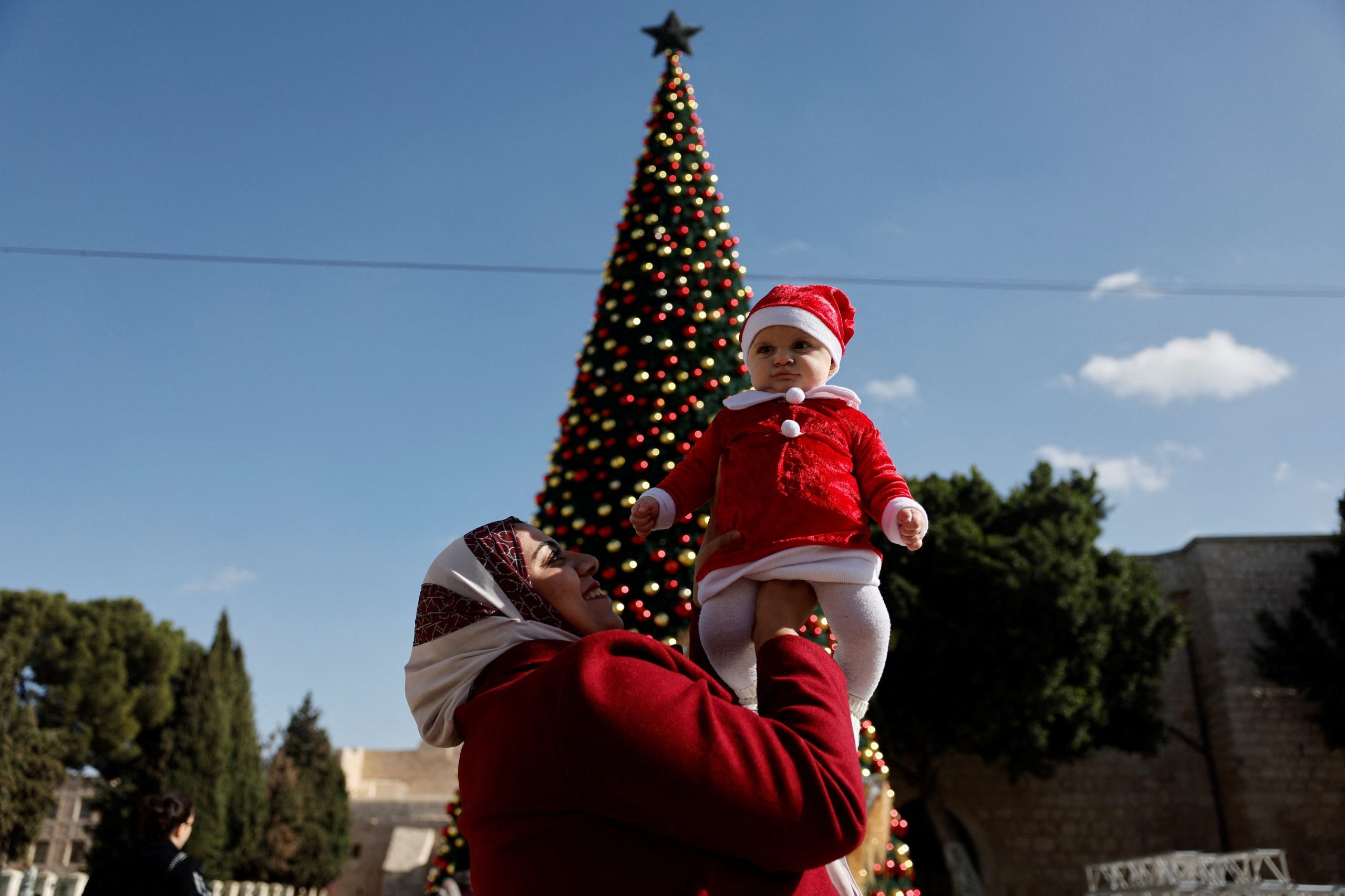 Hamamreh sostiene a Arine, su hija de seis meses, frente a un árbol de Navidad en la Plaza del Pesebre en Belén