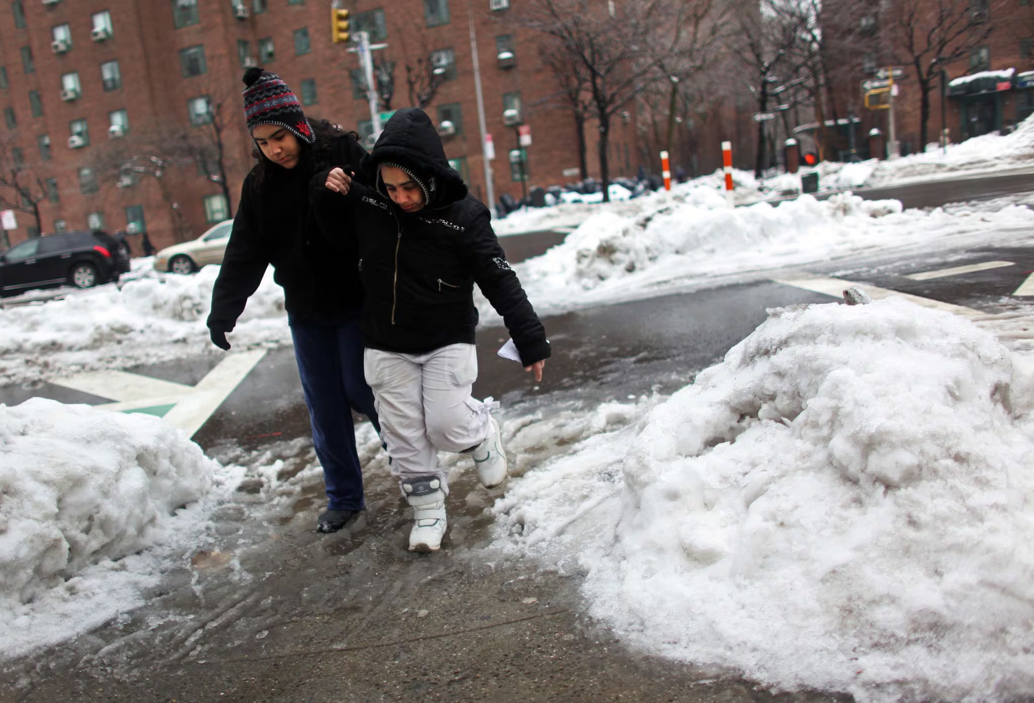 Peatones cruzan una calle con acumulación de nieve y hielo, en un contexto de advertencias oficiales sobre el peligro del hielo negro en la calzada