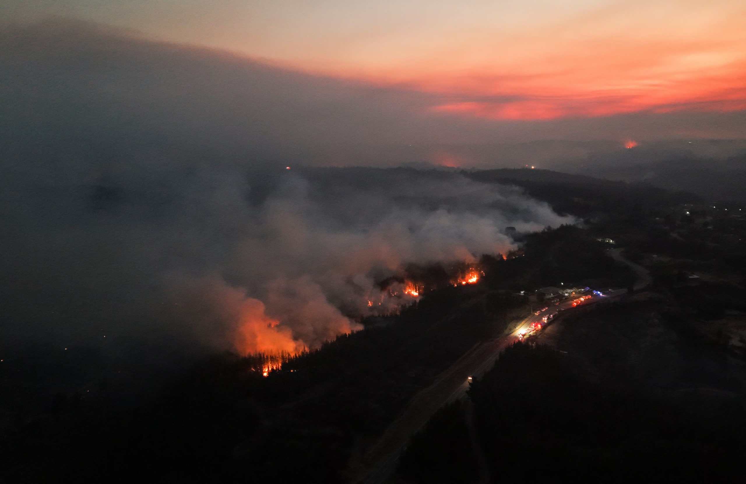 Vista aérea de vehículos de bomberos y rescate estacionados a lo largo de una carretera mientras un incendio forestal arde en la región del Biobío, donde múltiples incendios forestales han provocado evacuaciones de emergencia, en Florida, Chile, el 21 de enero de 2026 (REUTERS/Adriano Machado)