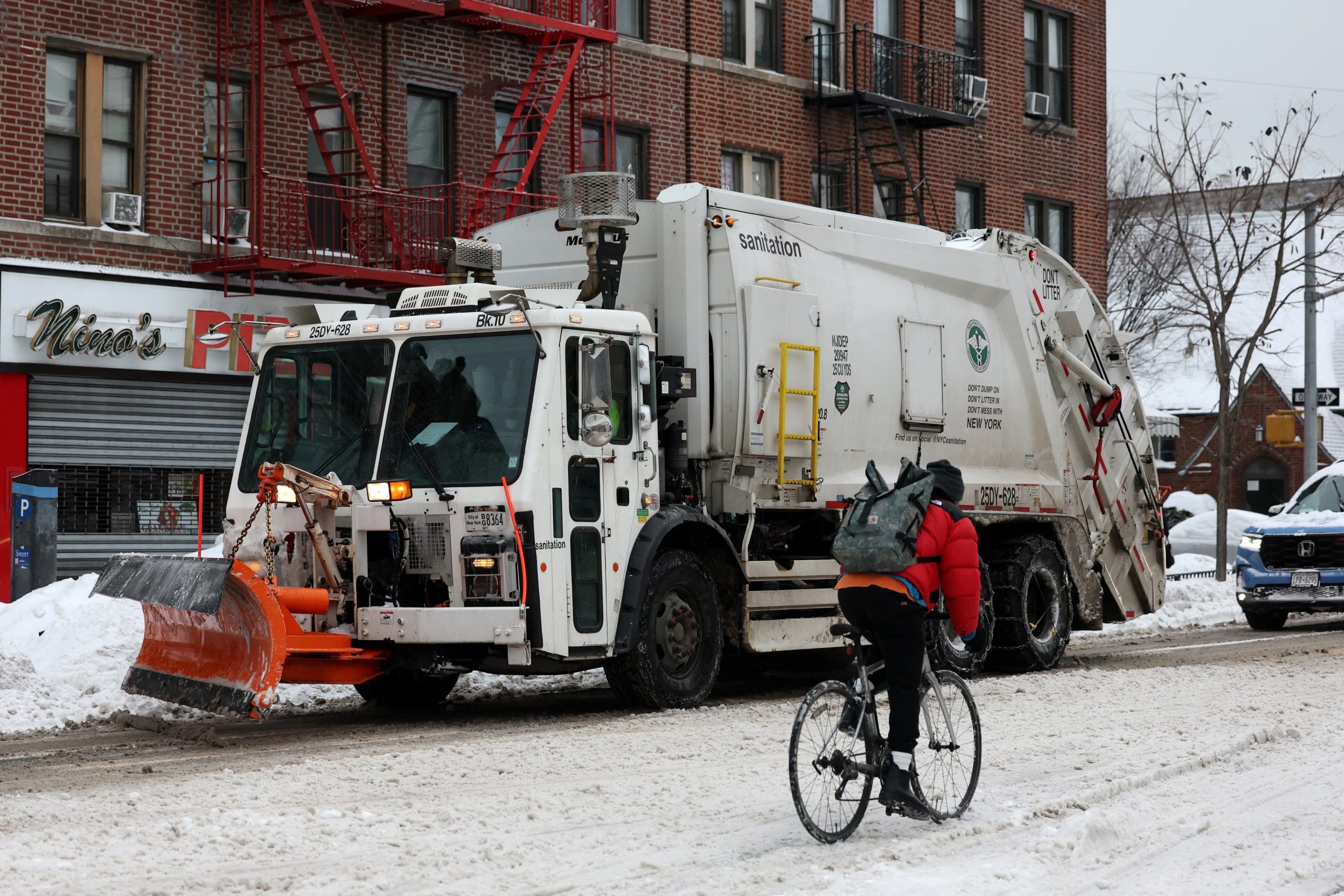Un hombre monta en bicicleta por una calle nevada junto a un camión de basura del Departamento de Sanidad de Nueva York con una pala quitanieves. REUTERS/Brendan McDermid