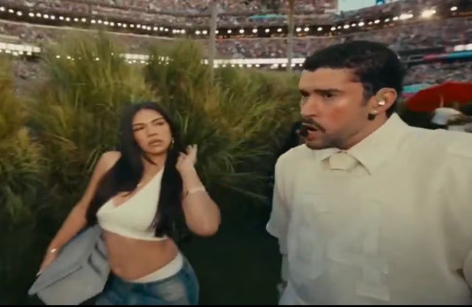 La bailarina Kandrex Millones y el artista Bad Bunny son vistos caminando entre la vegetación con una multitud de personas de fondo, generando expectación entre los presentes (ESPN)