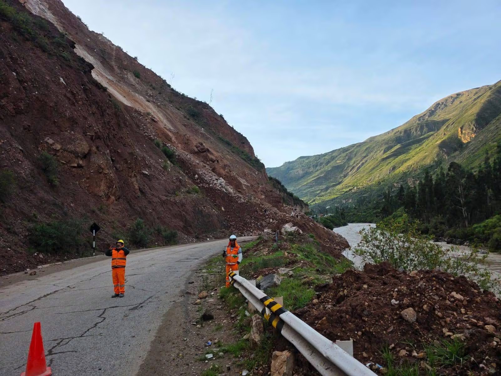 Dos trabajadores de mantenimiento vial observan un deslizamiento de tierra que ha bloqueado parcialmente una carretera de montaña junto a un río (Foto: Noticias con Calle)