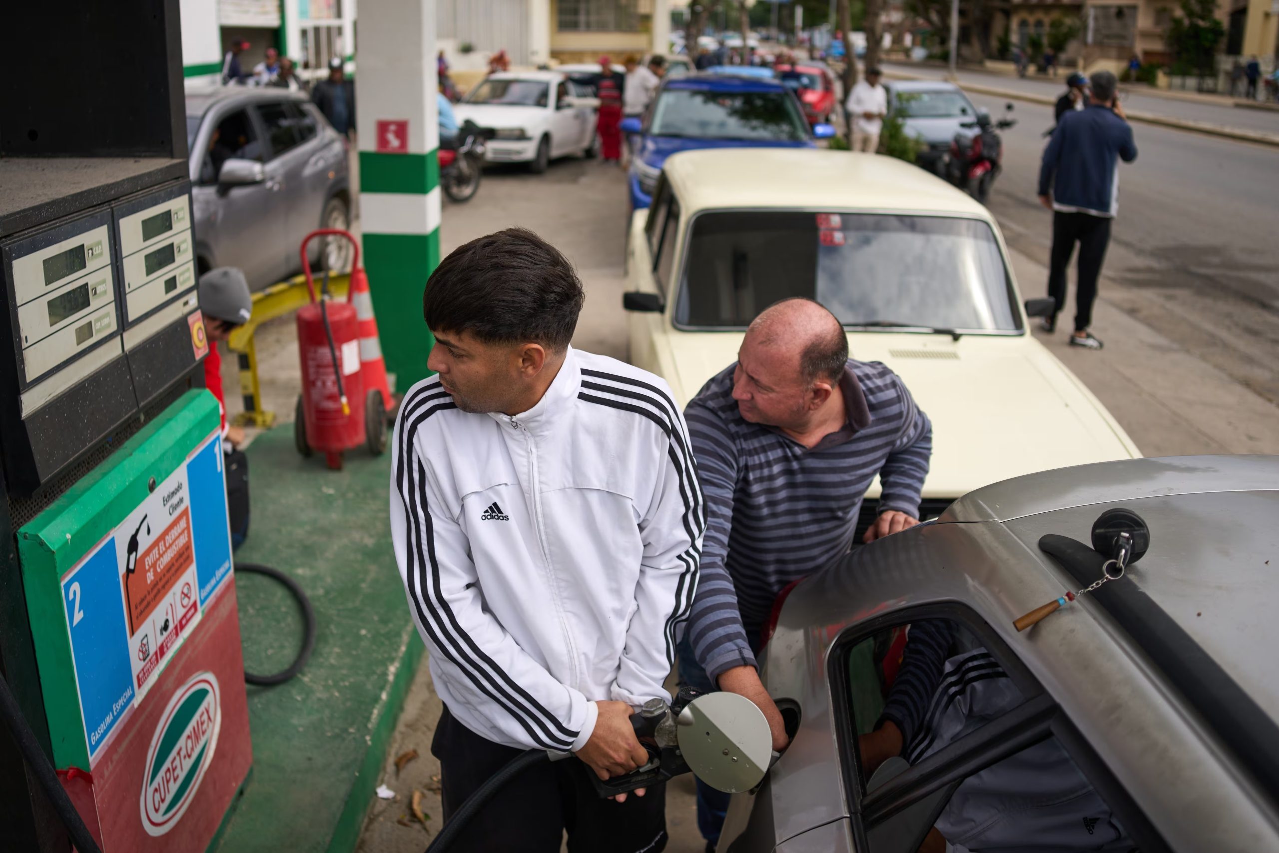 Personas repostan en una gasolinera mientras otros esperan detrás en una larga fila en La Habana, Cuba, el viernes 30 de enero de 2026 (AP Foto/Ramón Espinosa)