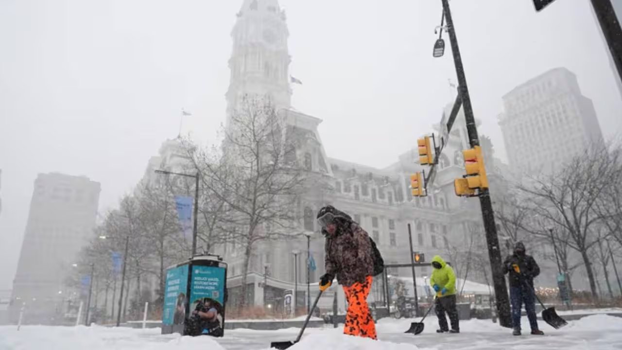 Varios residentes palean la nieve de las aceras frente a edificios históricos en medio de una fuerte ventisca invernal que azota la ciudad.