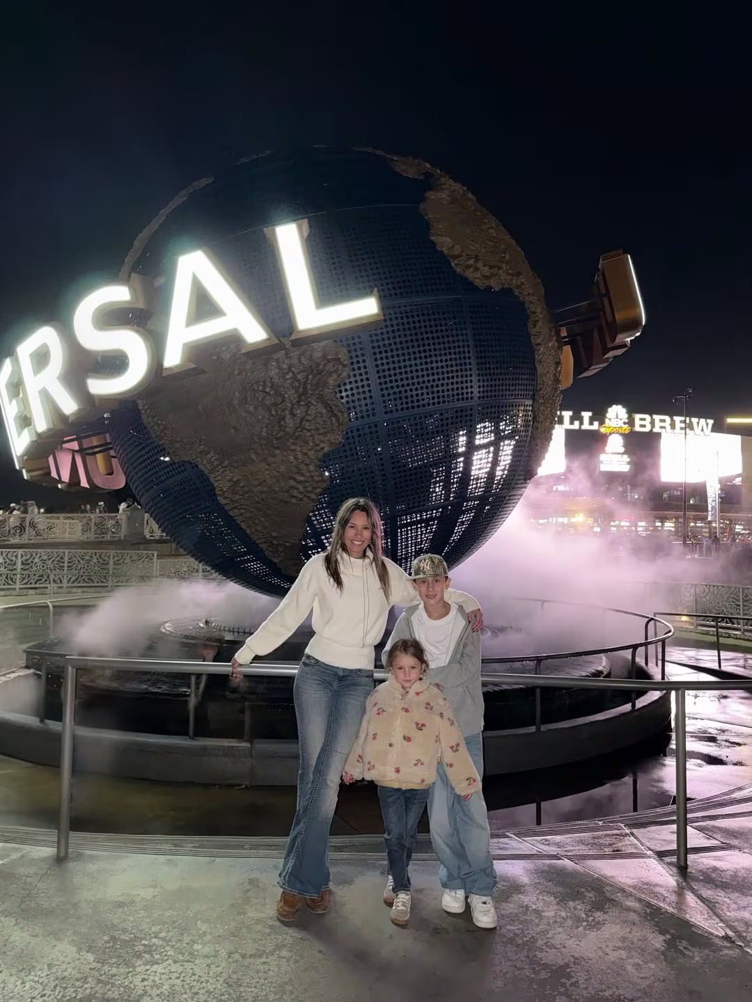 Pampita posa sonriente con sus hijos Anita García Moritán y Benicio Vicuña frente al icónico globo de Universal Studios, disfrutando de una noche mágica en el parque temático (Instagram)