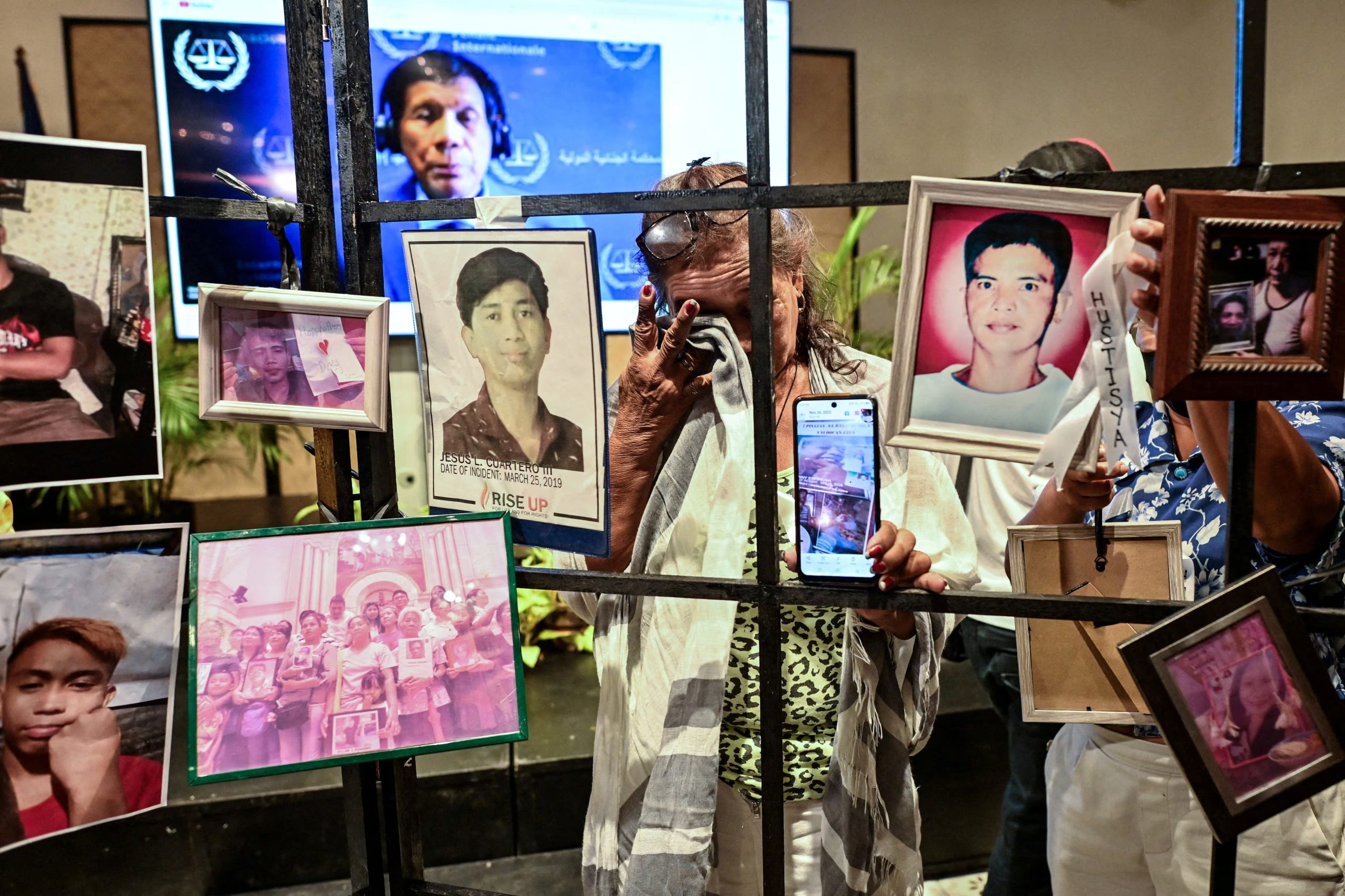 María Espinosa, madre de una víctima de la guerra contra el narcotráfico, llora mientras muestra una foto de su hijo fallecido, junto con las fotos de otras víctimas, minutos antes del comienzo de la audiencia del ex presidente filipino Rodrigo Duterte
REUTERS/Noel Celis