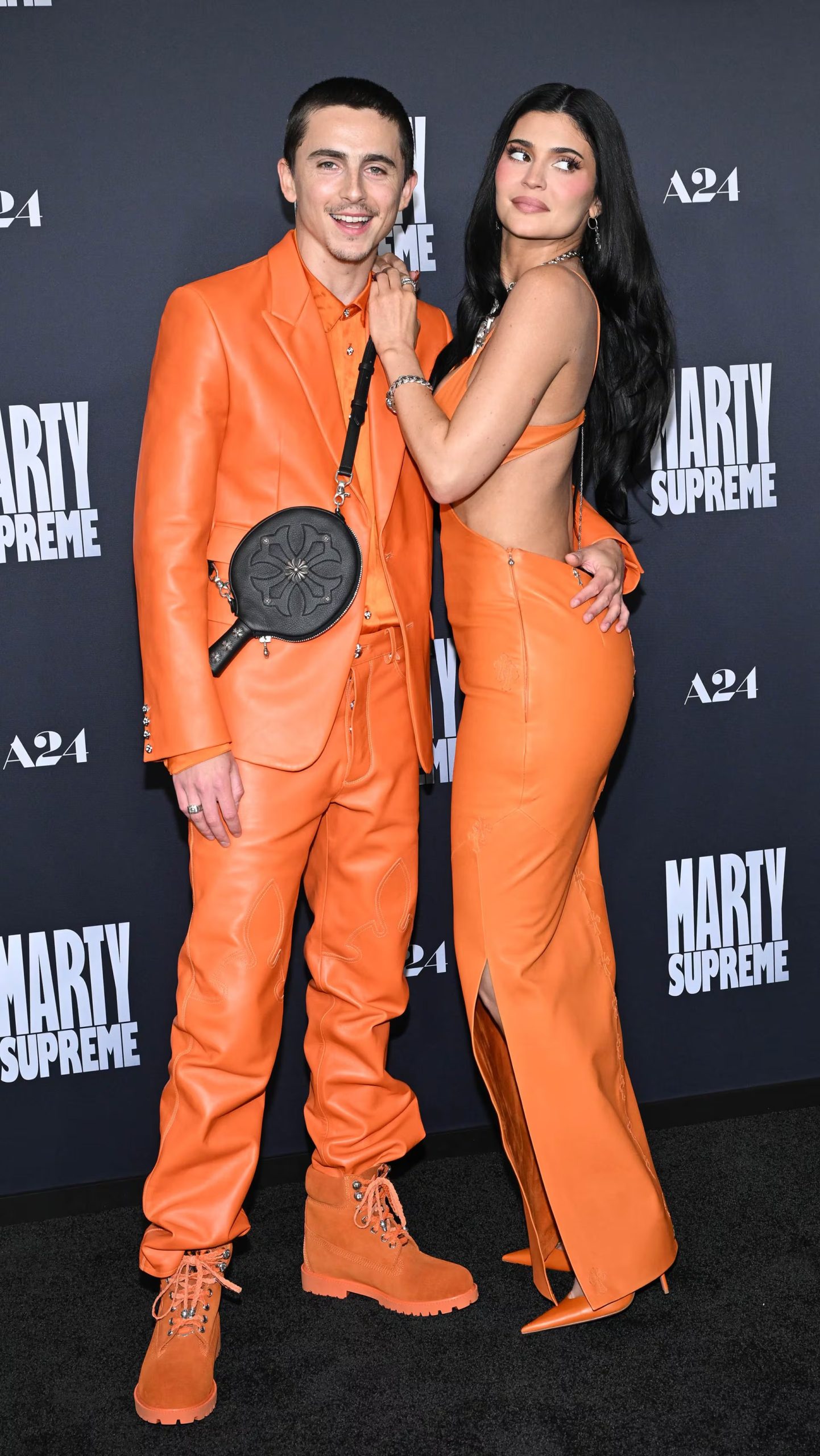 Impacto visual con atuendos de cuero naranja y accesorios plateados en la premiere de Marty supreme (Grosby)