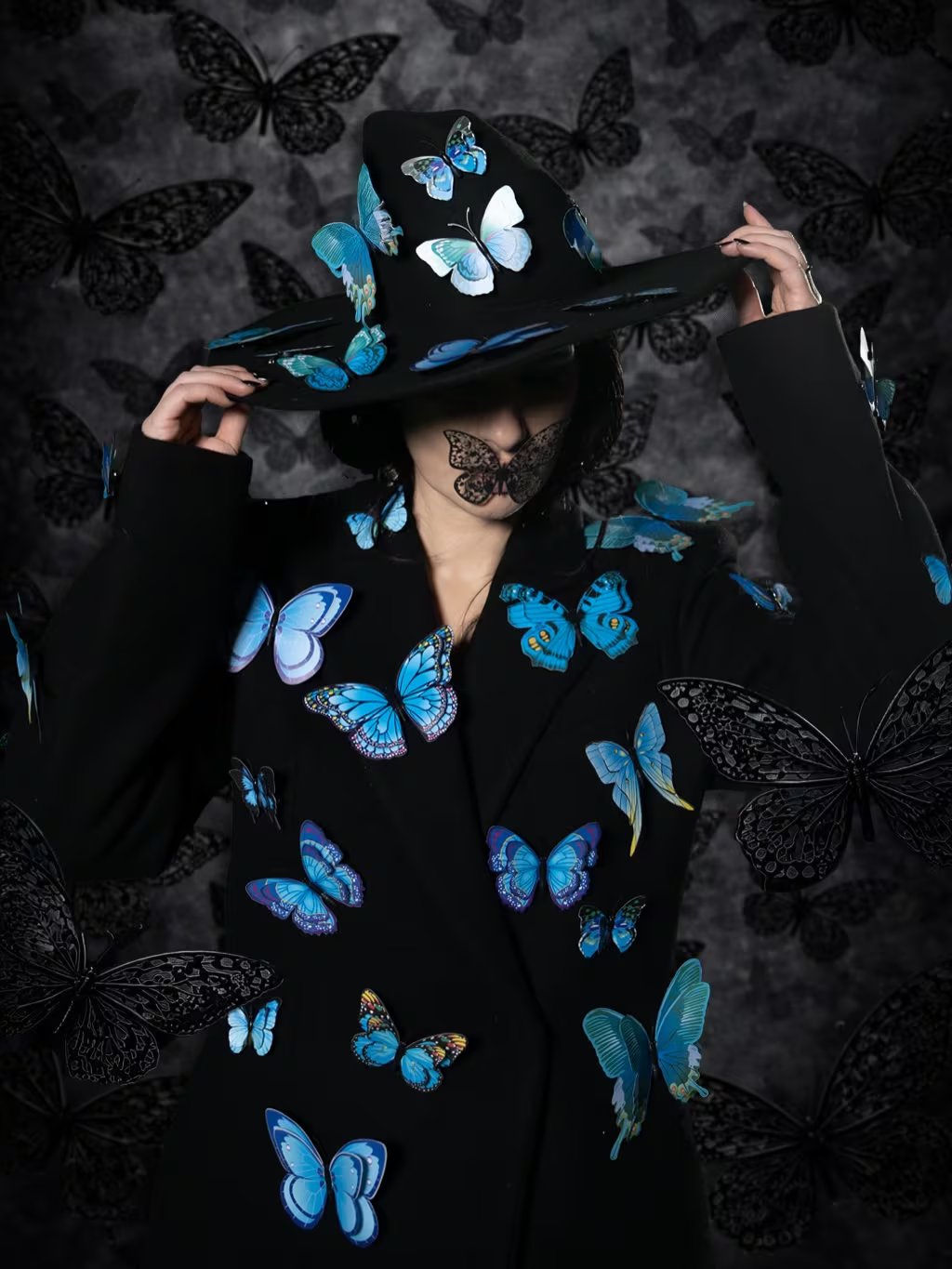 Laura Pausini posa con un sombrero y un abrigo negros adornados con mariposas azules vibrantes, en las fotos promocionales de su reversión de 