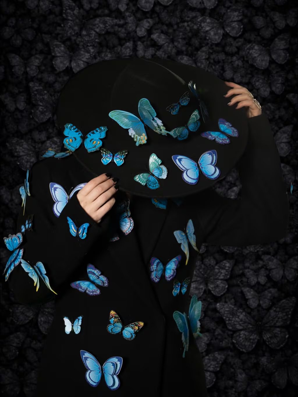 Laura Pausini posa con un sombrero y un abrigo negros adornados con mariposas azules vibrantes, en las fotos promocionales de su reversión de 