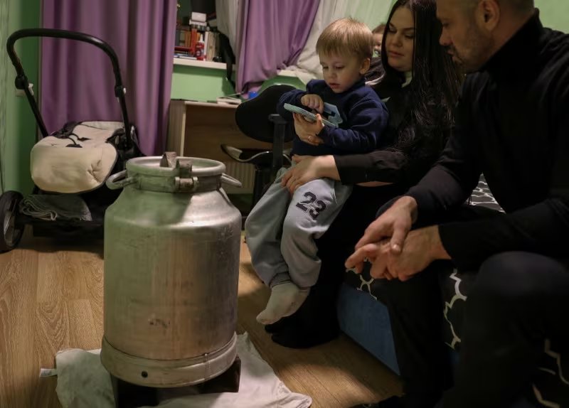 Anton Rybikov, de 39 años, su esposa Marina y sus hijos David y Matvii se calientan alrededor de una batidora de metal con agua caliente durante un apagón (REUTERS/Anatolii Stepanov)