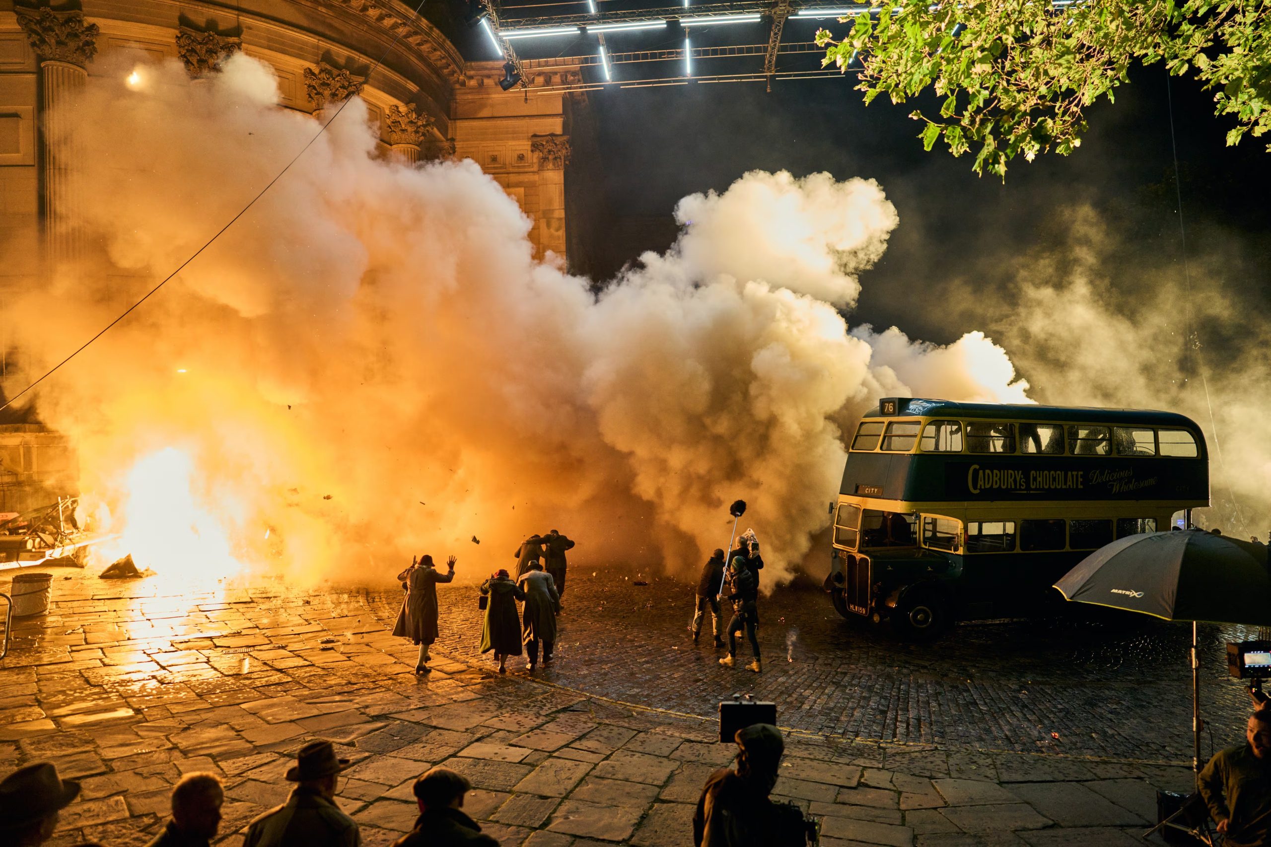 Una espectacular explosión se produce durante la filmación de 'Peaky Blinders: The Immortal Man', con figuras vestidas de época y un autobús antiguo en medio del caos y el humo denso. (Netflix)