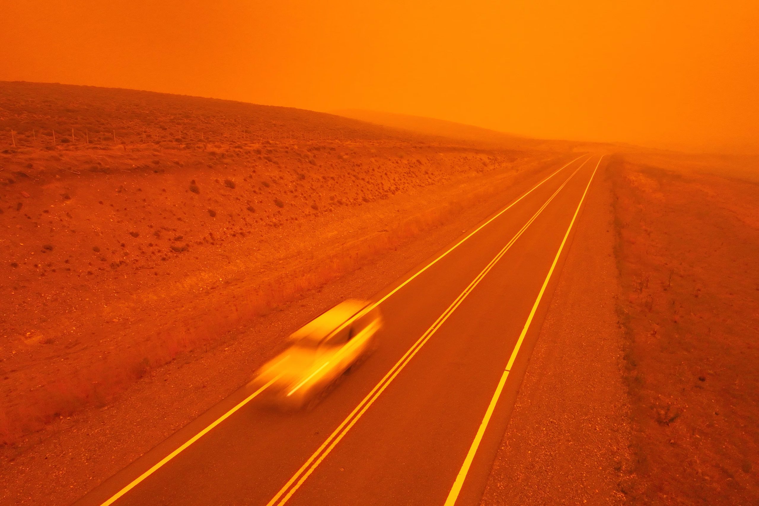 Un automóvil avanza a toda velocidad por una carretera mientras el humo de los incendios forestales tiñe de rojo el cielo cerca de Cholila, Argentina, el domingo 1 de febrero de 2026. (Foto AP/Victor R. Caivano)