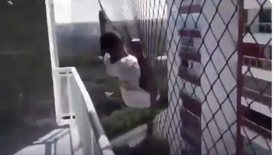 Un trabajador realiza la instalación de una ventana en un edificio alto, utilizando una red de seguridad como medida de protección.