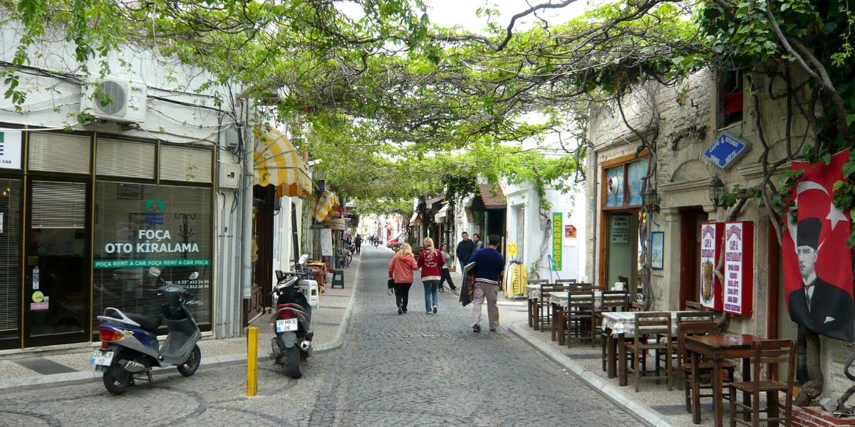 Las tradiciones vivas de Eski Foça se reflejan en el mercado local Yeryüzü Pazarı, la arquitectura de casas griegas y las cenas de mariscos frente al mar en bistrós históricos (Wikipedia)