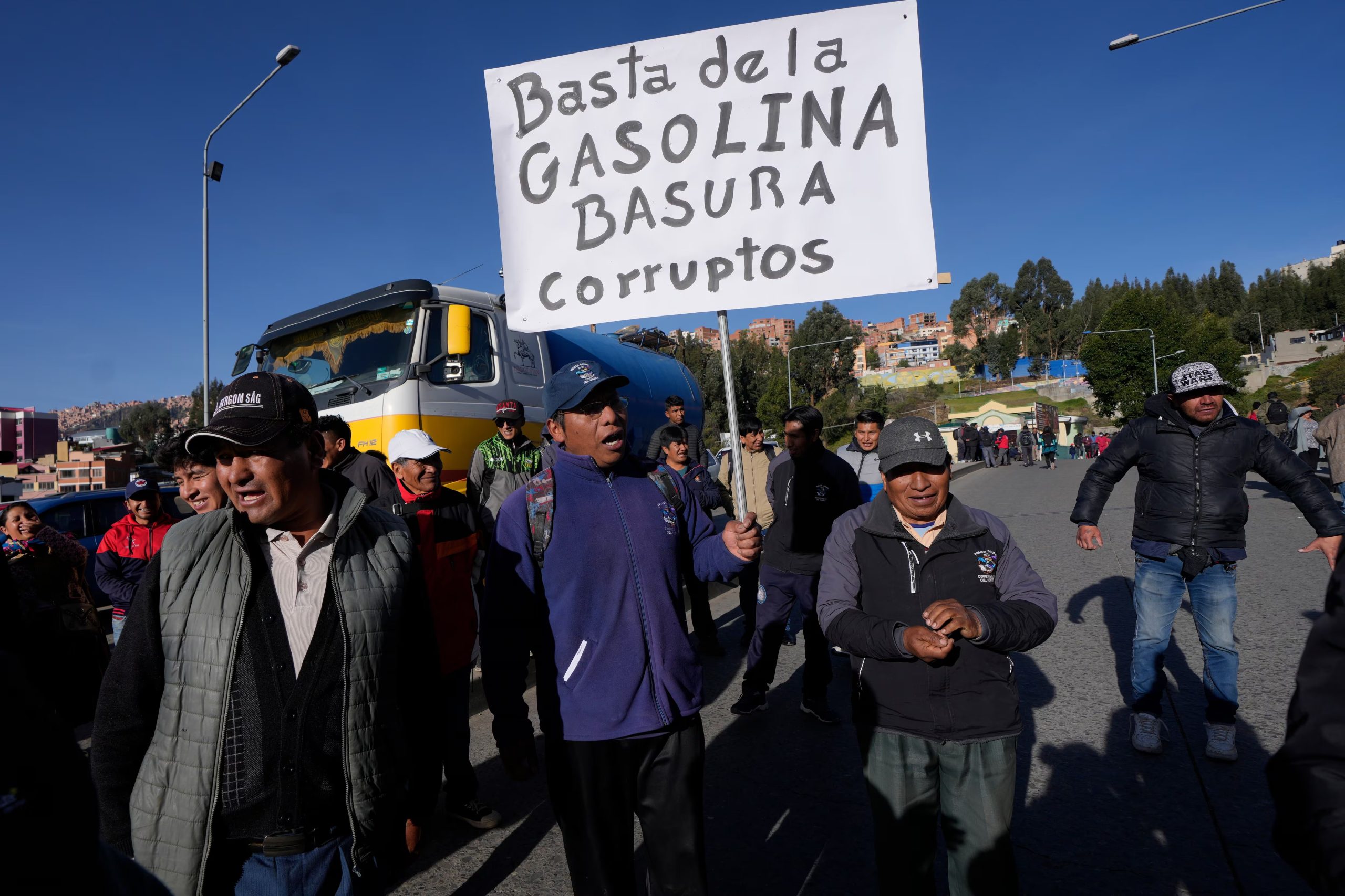 Conductores del transporte público protestan por la mala calidad de la gasolina; uno de ellos sostiene un cartel en el que se lee en español