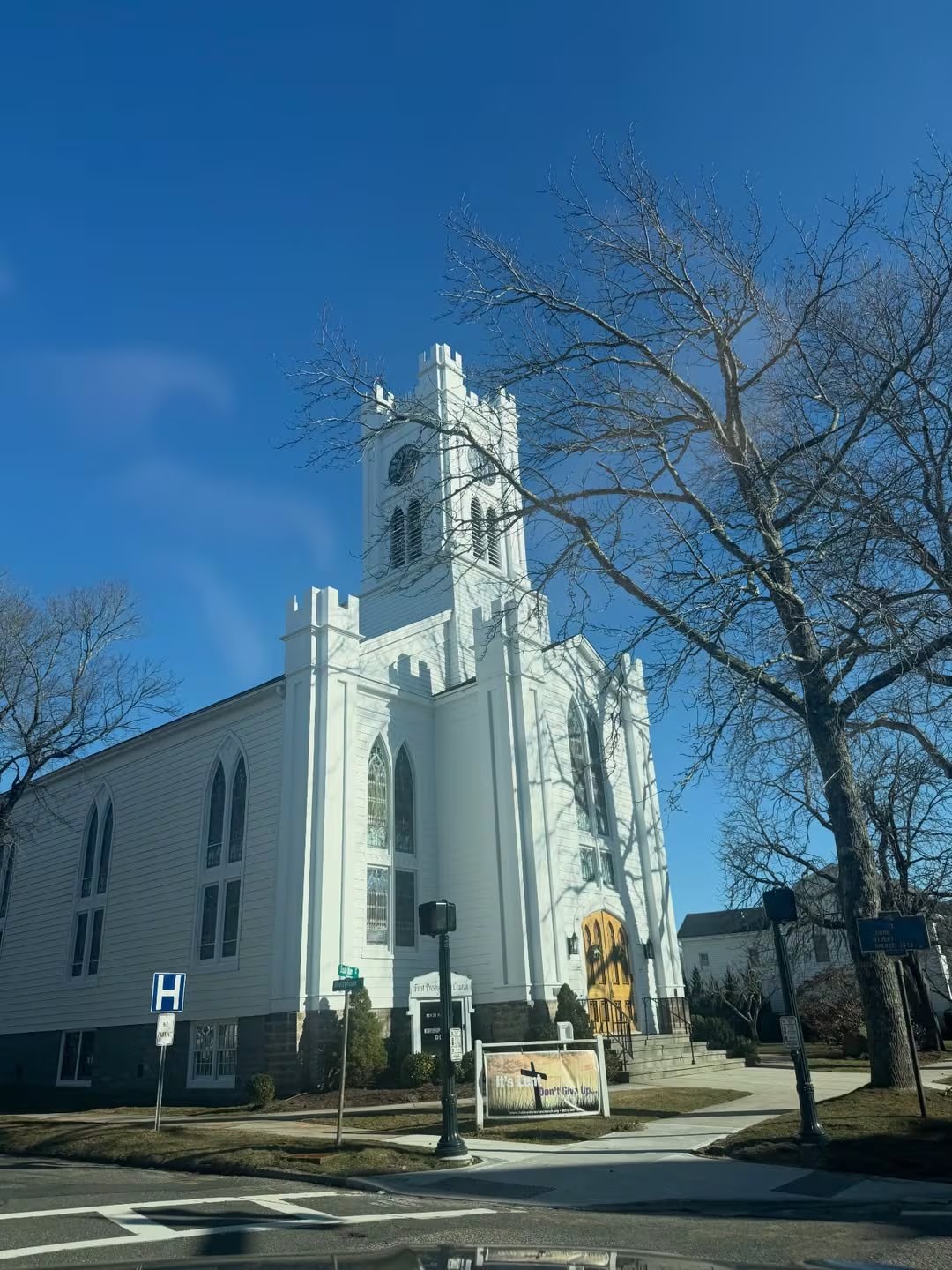 Una iglesia presbiteriana de fachada blanca y arquitectura clásica se erige majestuosa bajo un cielo azul claro, flanqueada por árboles sin hojas, en un día soleado de otoño en Nueva York