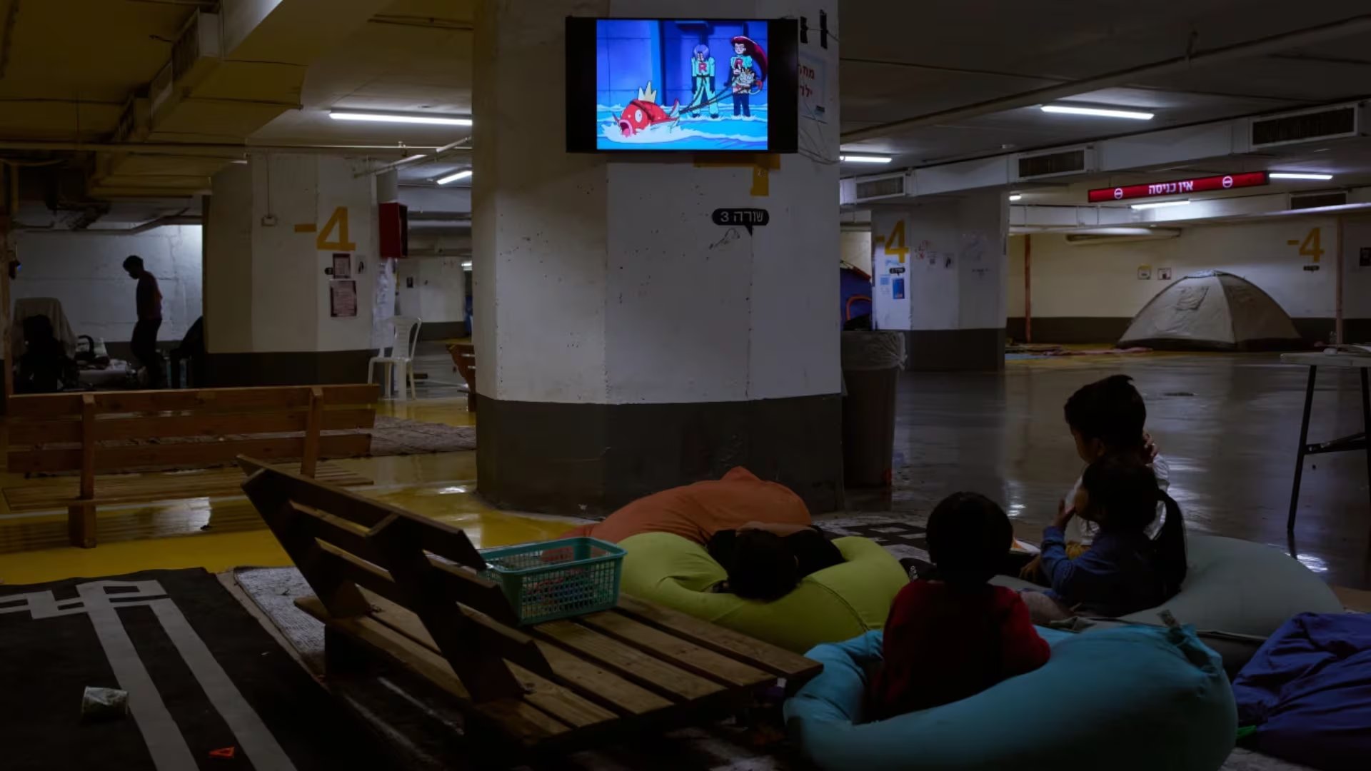 Niños ven la televisión en un estacionamiento subterráneo donde la gente pasa la noche como medida de precaución ante posibles ataques con misiles iraníes en Tel Aviv, Israel, el jueves 12 de marzo de 2026 (AP/Oded Balilty)