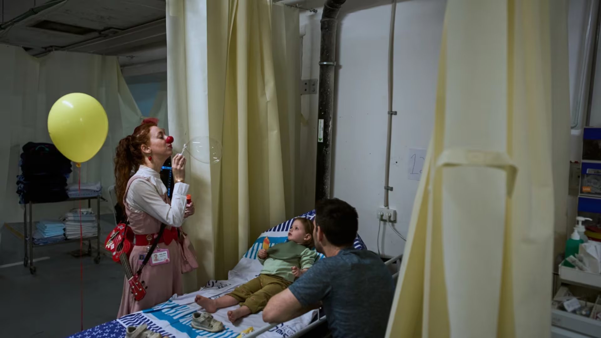 Un miembro del personal médico entretiene a un joven paciente en una sala de urgencias provisional instalada en un estacionamiento subterráneo utilizado como refugio bajo el Centro Médico Sheba en Ramat Gan, Israel, el martes 17 de marzo de 2026 (AP/Oded Balilty)