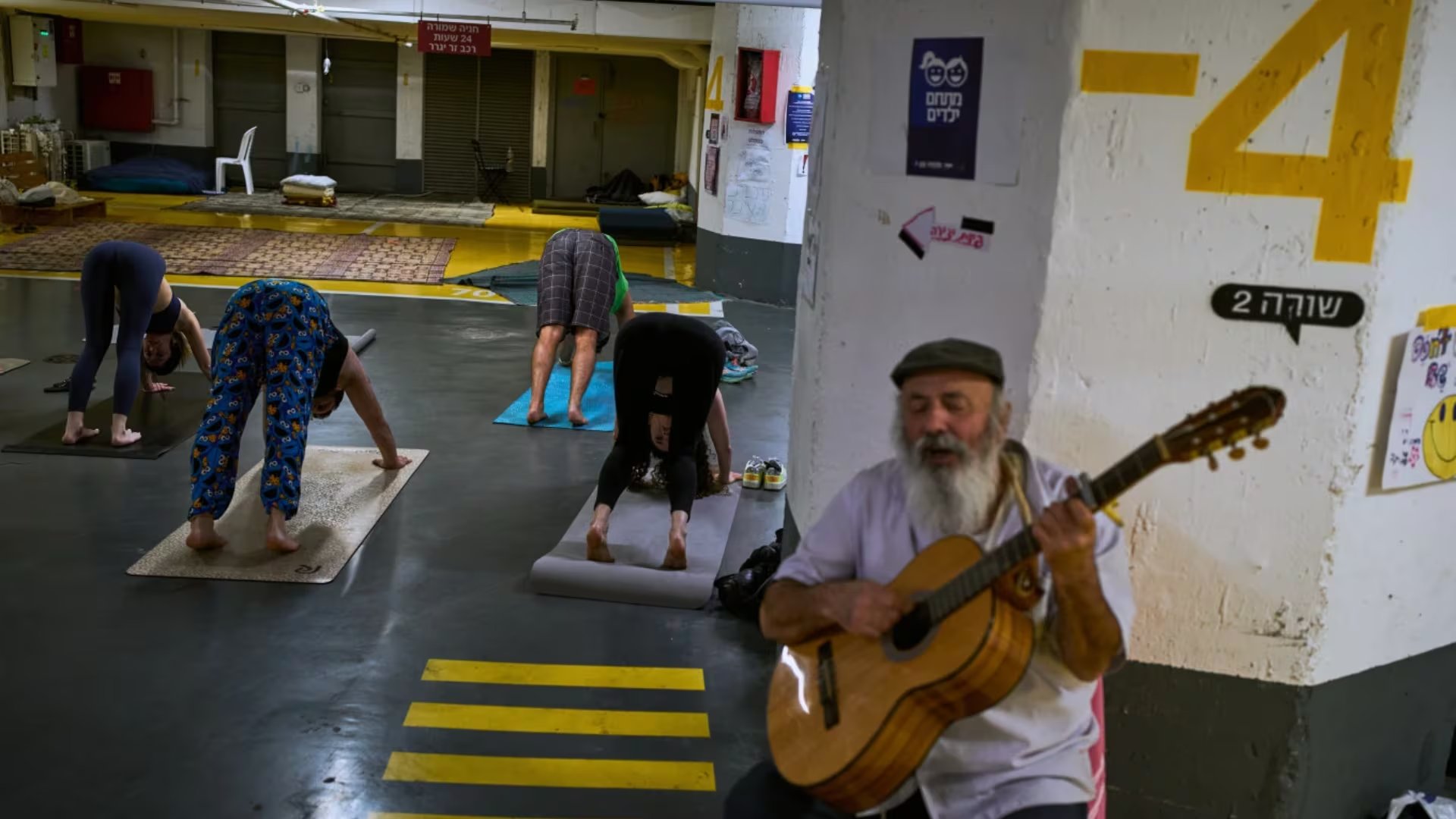 Un hombre toca la guitarra mientras varias personas asisten a una clase de yoga en un estacionamiento subterráneo utilizado como refugio contra posibles ataques con misiles iraníes en Tel Aviv, Israel, el martes 17 de marzo de 2026 (AP/Oded Balilty)