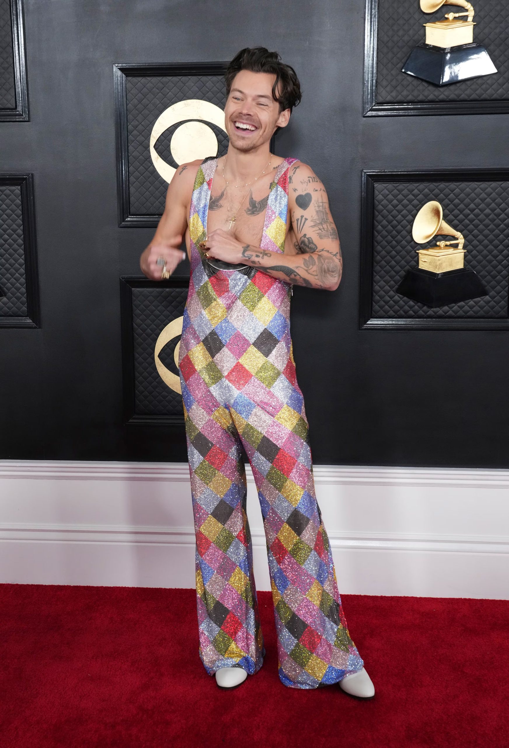 El mono largo de lentejuelas con rombos multicolor y zapatos blancos fue el sello distintivo de Harry Styles en otra alfombra roja (Jordan Strauss/Invision/AP)