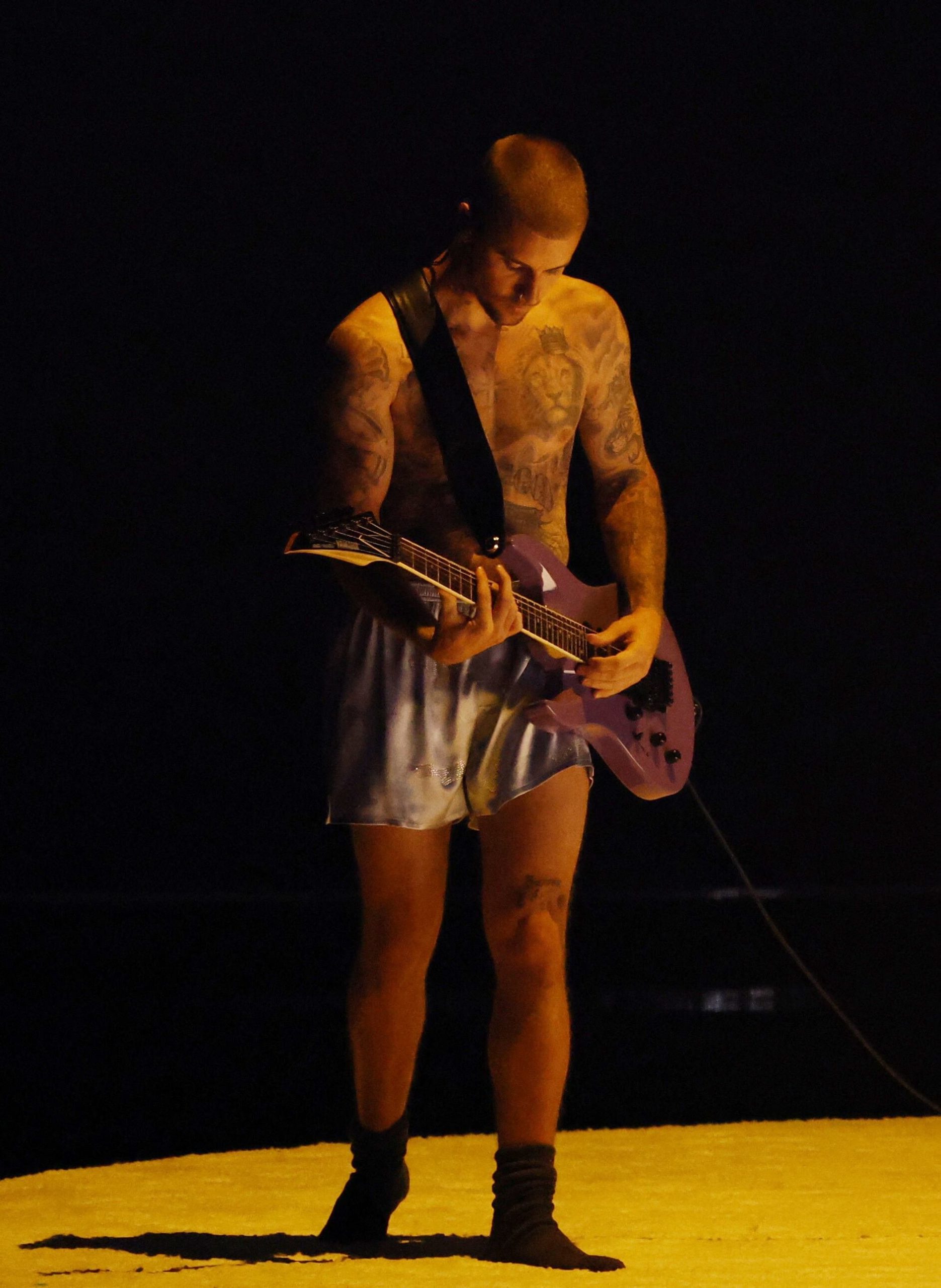 El short satinado plateado y la guitarra violeta destacan la actitud despreocupada y artística de Justin Bieber, convirtiendo un atuendo minimalista en una declaración de personalidad y creatividad (REUTERS/Daniel Cole)