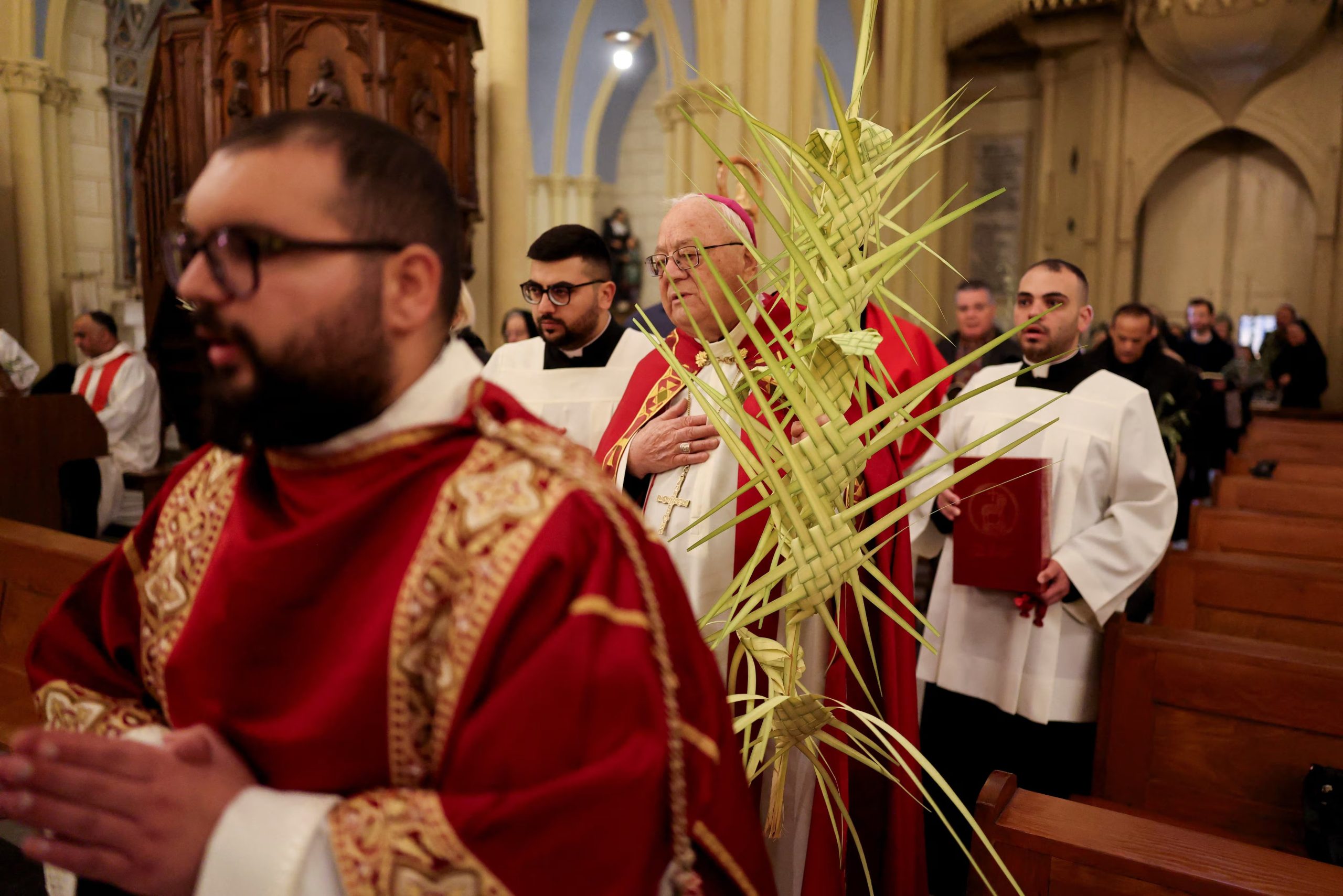 Fieles cristianos celebran el Domingo de Ramos en el Patriarcado Latino de Jerusalén, en la Ciudad Vieja. La tradicional procesión desde el Monte de los Olivos, que cada año convoca a miles de peregrinos, fue cancelada por las restricciones de la guerra. (REUTERS/Ammar Awad)