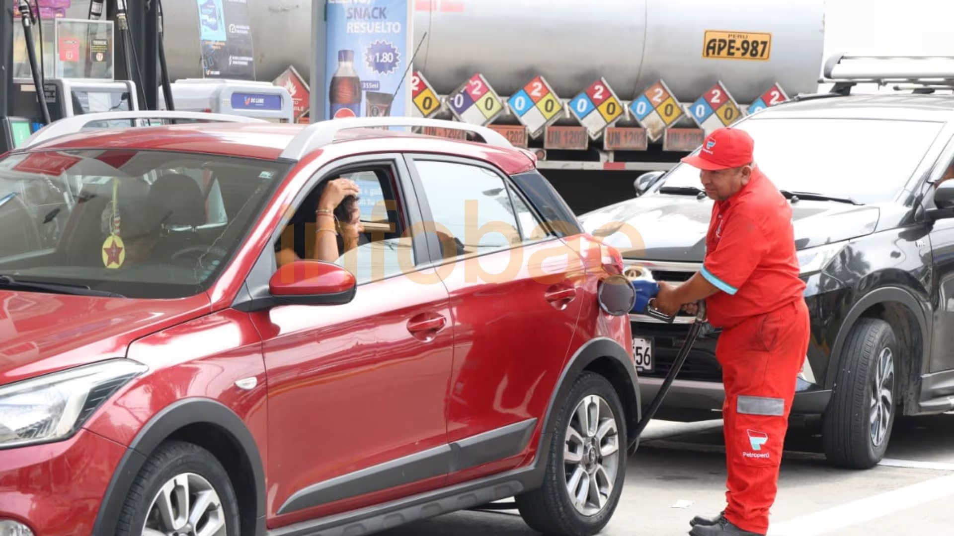 Un trabajador de una estación de servicio llena el tanque de un SUV rojo mientras otro vehículo espera detrás, con un camión cisterna en el fondo. (Paula Elizalde / Infobae Perú)