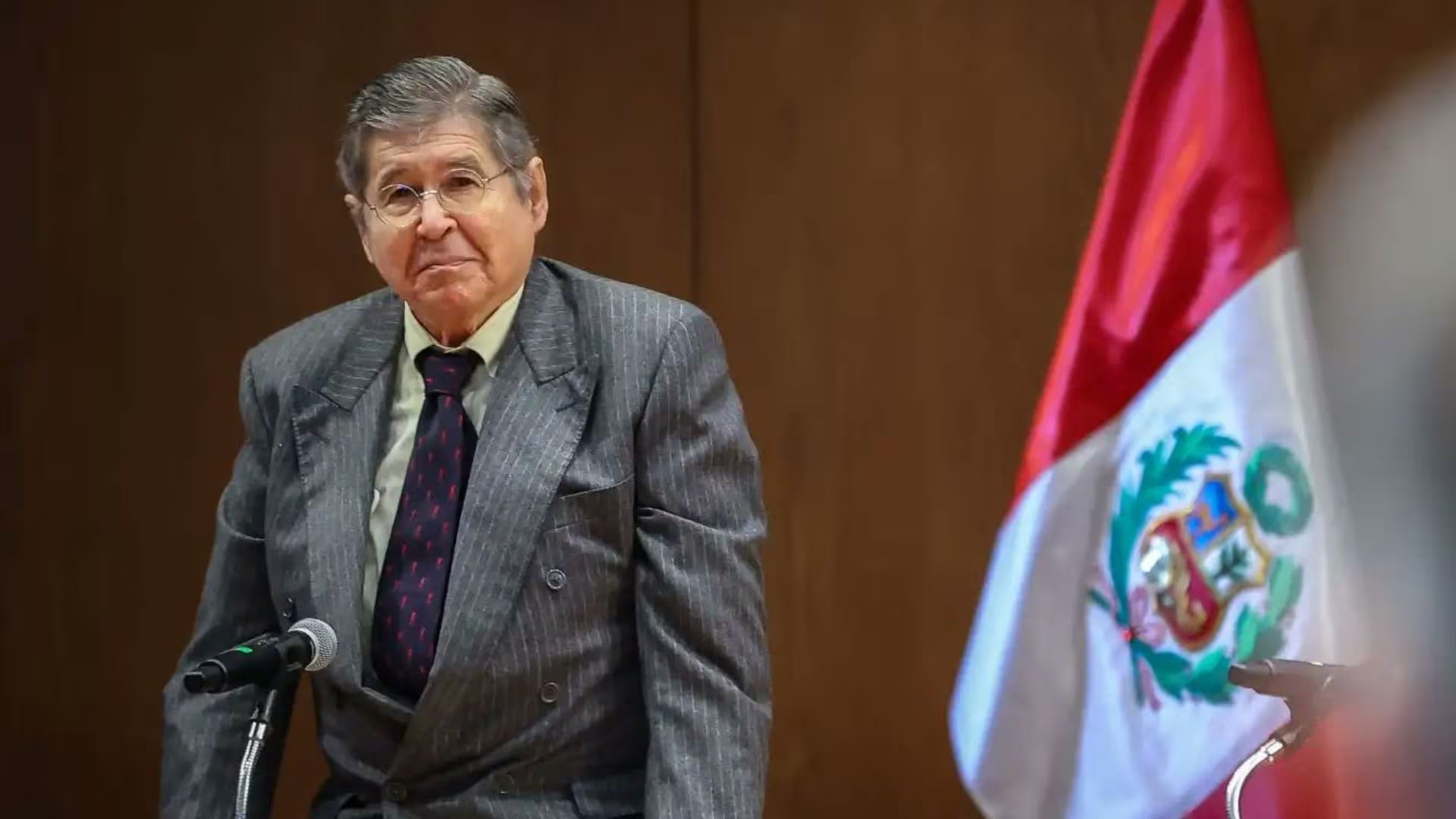 El reconocido escritor peruano Alfredo Bryce Echenique posa frente a la bandera de Perú en una imagen de archivo, tras conocerse su fallecimiento a los 87 años. (Andina)