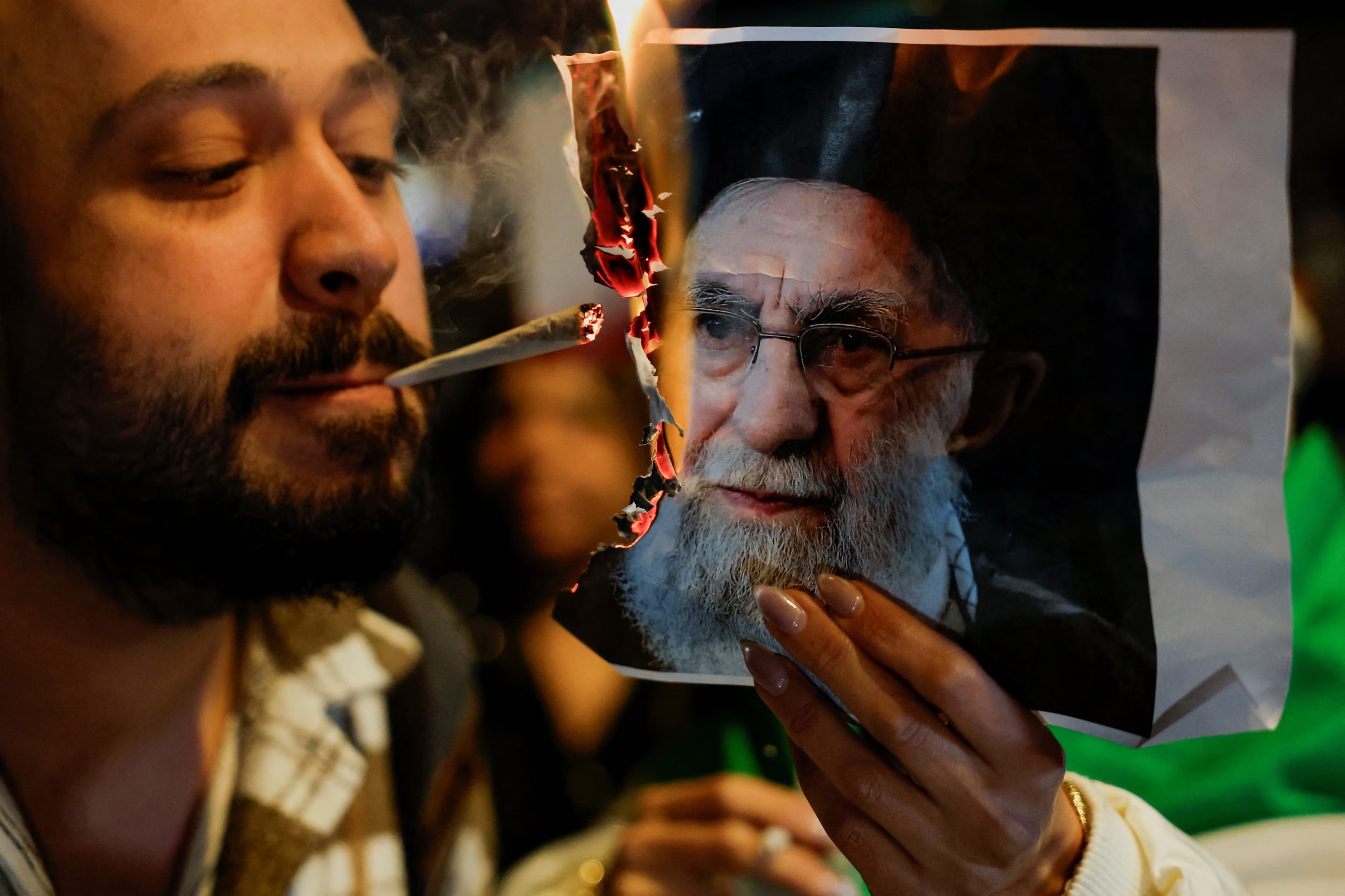 Manifestante prende un cigarrillo con una foto incendiada del depuesto líder iraní, Ali Khamenei durante una protesta en solidaridad con los manifestantes iraníes en Holon, Israel (REUTERS/Ammar Awad)