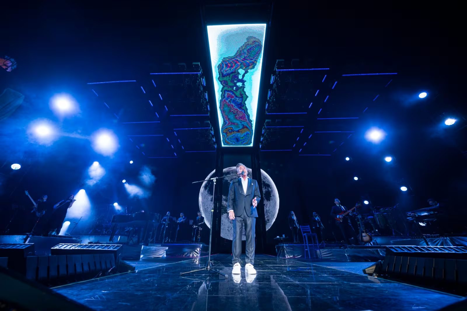 Ricardo Montaner canta en un escenario iluminado con luces azules y un fondo lunar, enviando un mensaje a sus fans peruanos antes de su concierto en Lima.