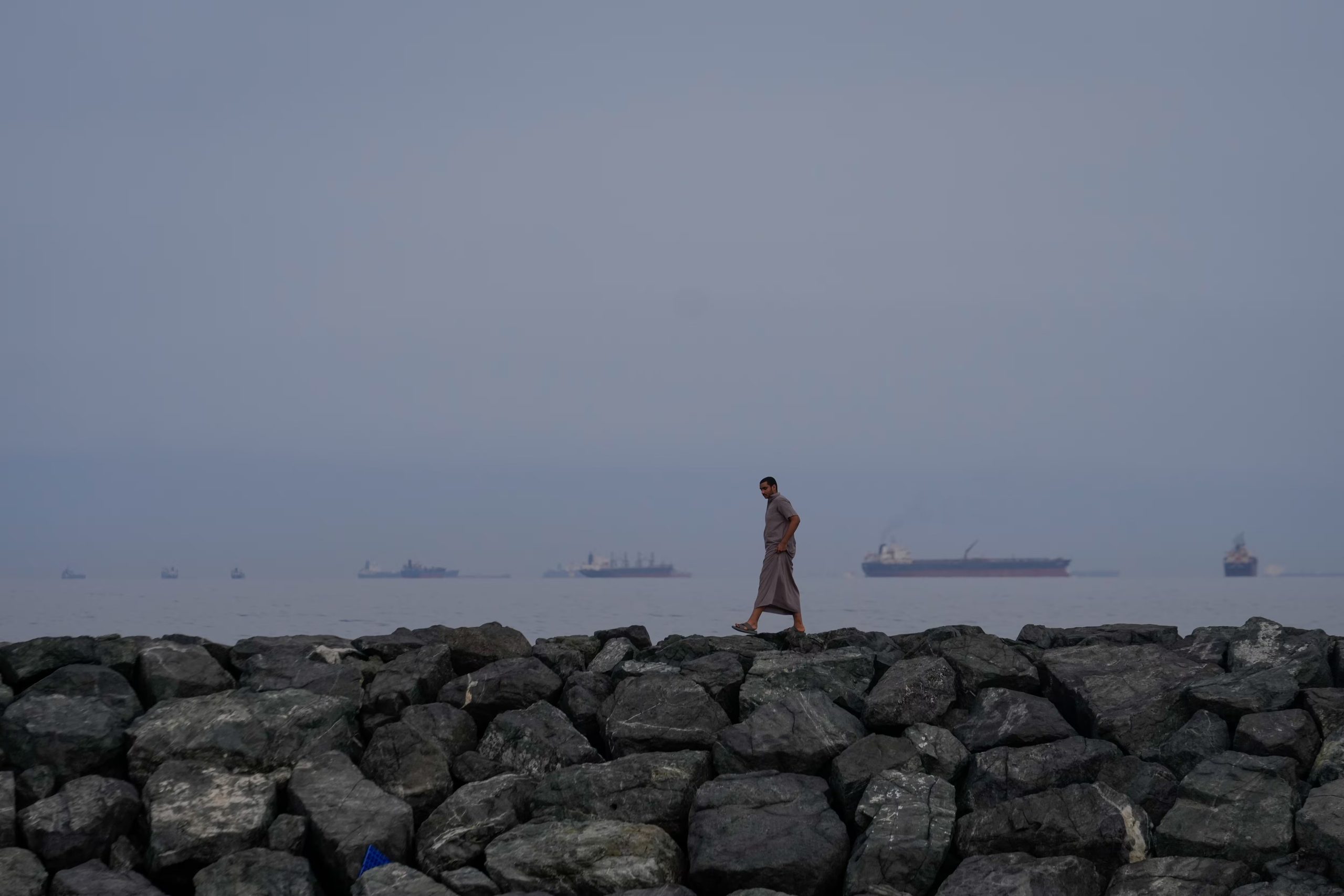 Un hombre camina por la orilla del mar mientras buques petroleros y de carga se alinean en el estrecho de Ormuz, vistos desde Khor Fakkan, Emiratos Árabes Unidos, el miércoles 11 de marzo de 2026 (AP Foto/Altaf Qadri/Archivo)
