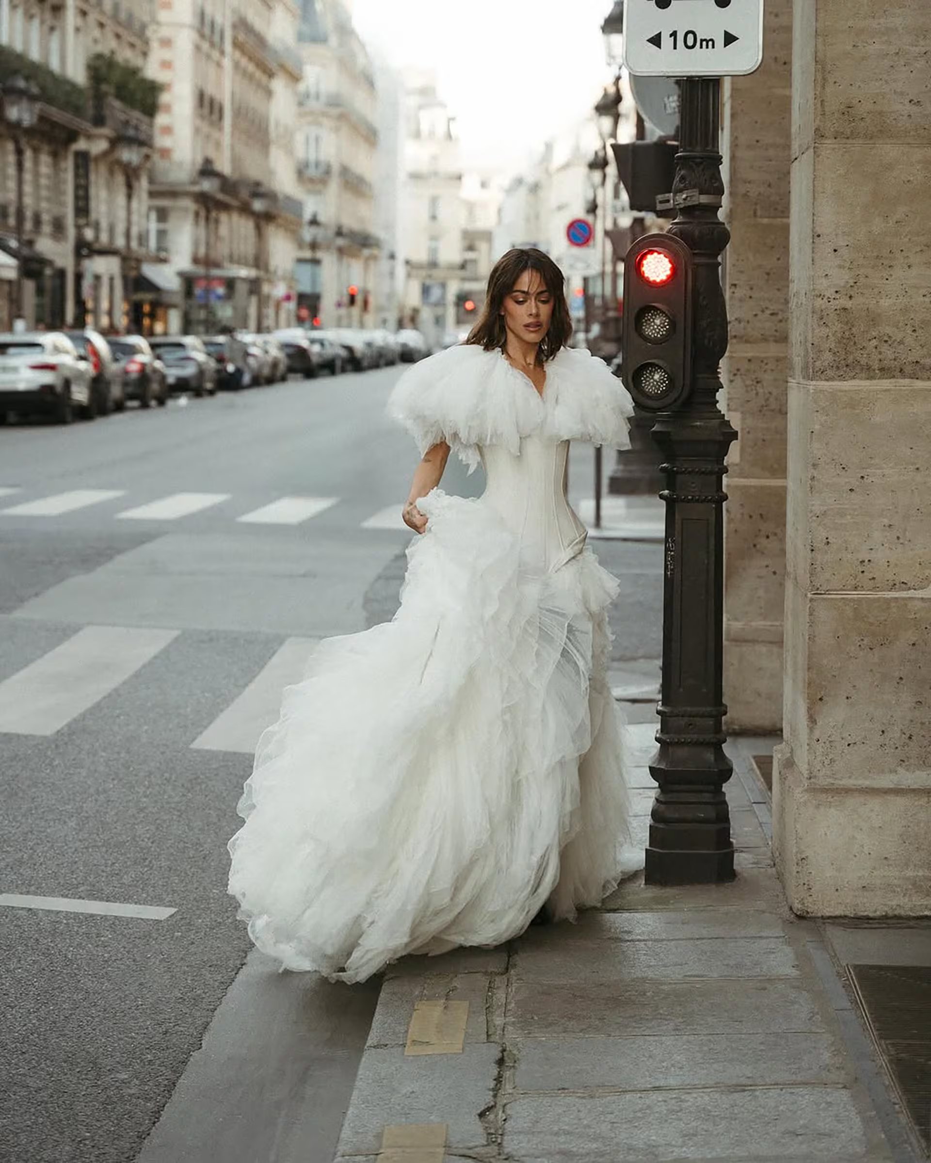 Desfilando por calles parisinas, la artista impacta con un vestido blanco de tul y capa de plumas