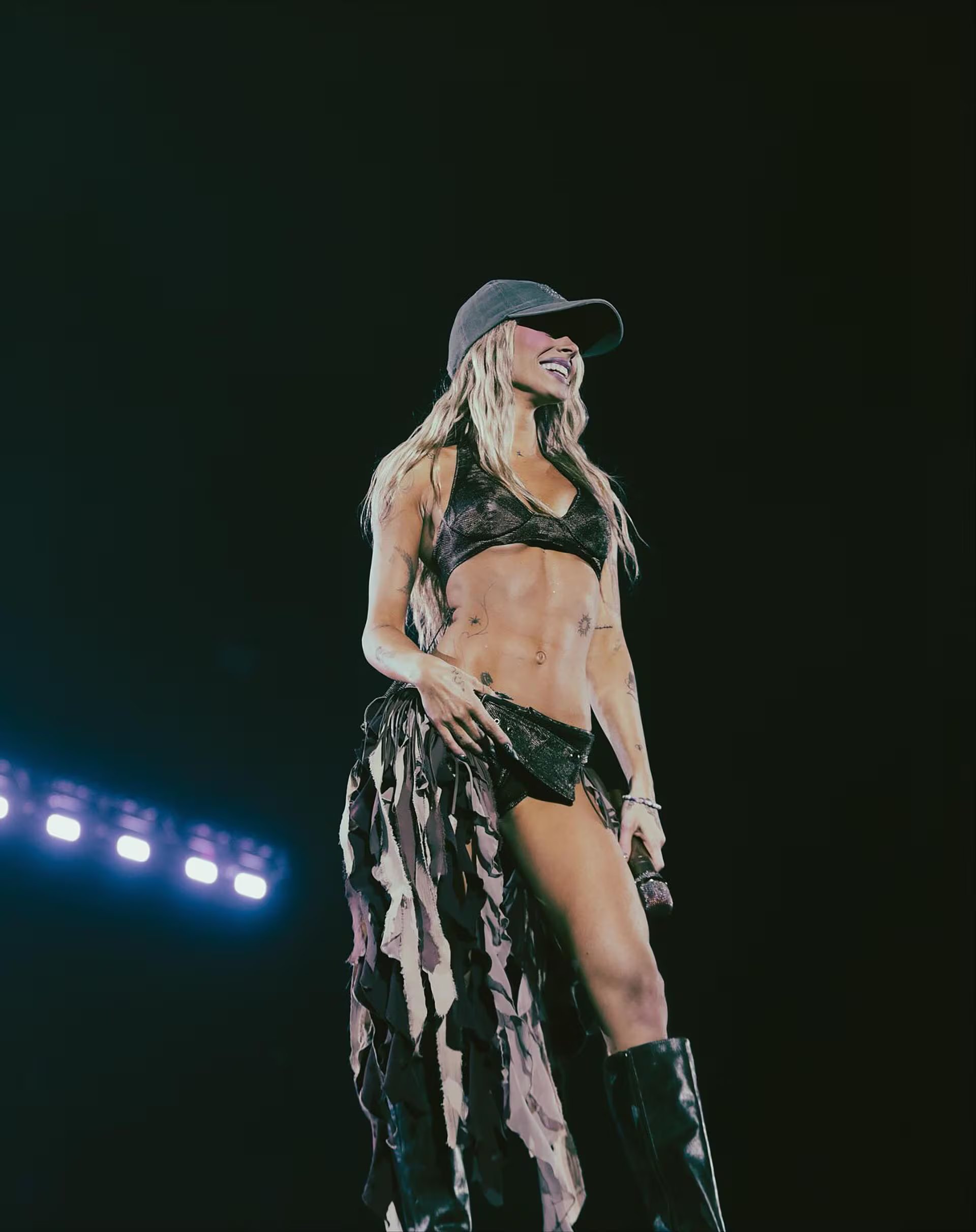 Durante su show, la artista sorprende con un top bikini y falda asimétrica, acompañados de botas altas, resaltando su actitud audaz y performática (Instagram: @tinistoessel)