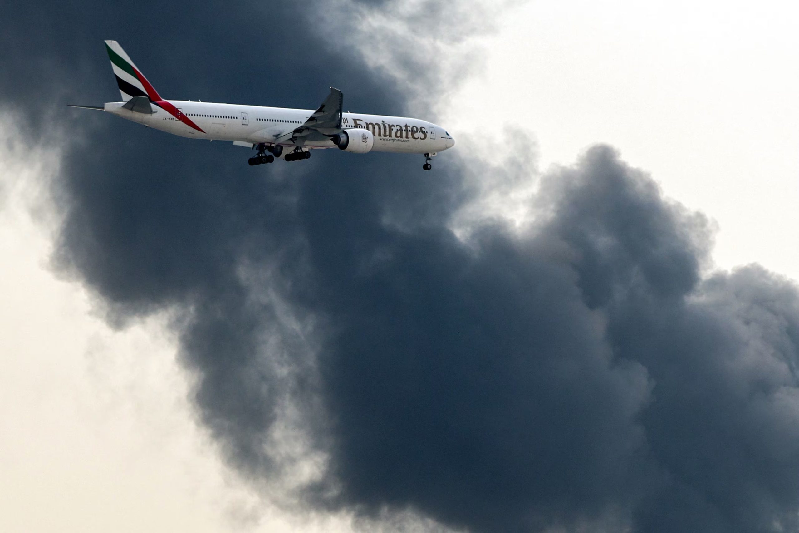 Un avión de Emirates se aproxima a la pista mientras una columna de humo se eleva desde las inmediaciones del Aeropuerto Internacional de Dubai tras el impacto de un dron en un tanque de combustible. Emirates pidió a los pasajeros que no se acercaran al aeropuerto hasta que se reanudaran las operaciones. (AFP)