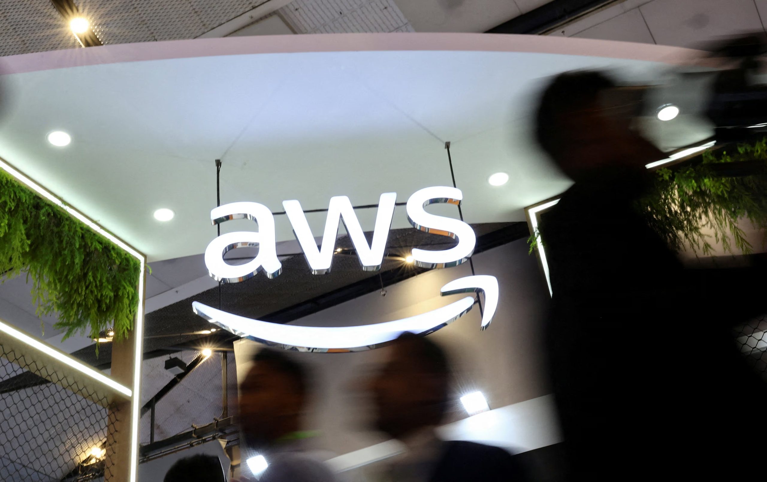 FILE PHOTO: People walk past the logo of Amazon Web Services (AWS) at its exhibitor stall at the India Mobile Congress 2025 at Yashobhoomi, a convention and expo center in New Delhi, India, October 8, 2025. REUTERS/Anushree Fadnavis/File Photo