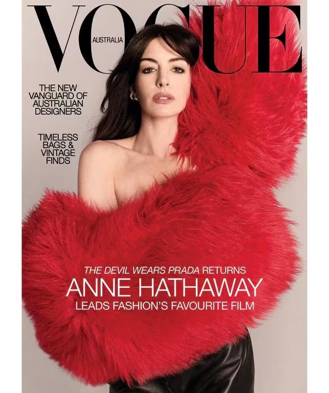 Anne Hathaway irrumpe en la portada de Vogue Australia envuelta en un abrigo de piel sintética rojo, con un hombro al descubierto y maquillaje neutro, en una imagen que fusiona presencia y vulnerabilidad (Vogue)