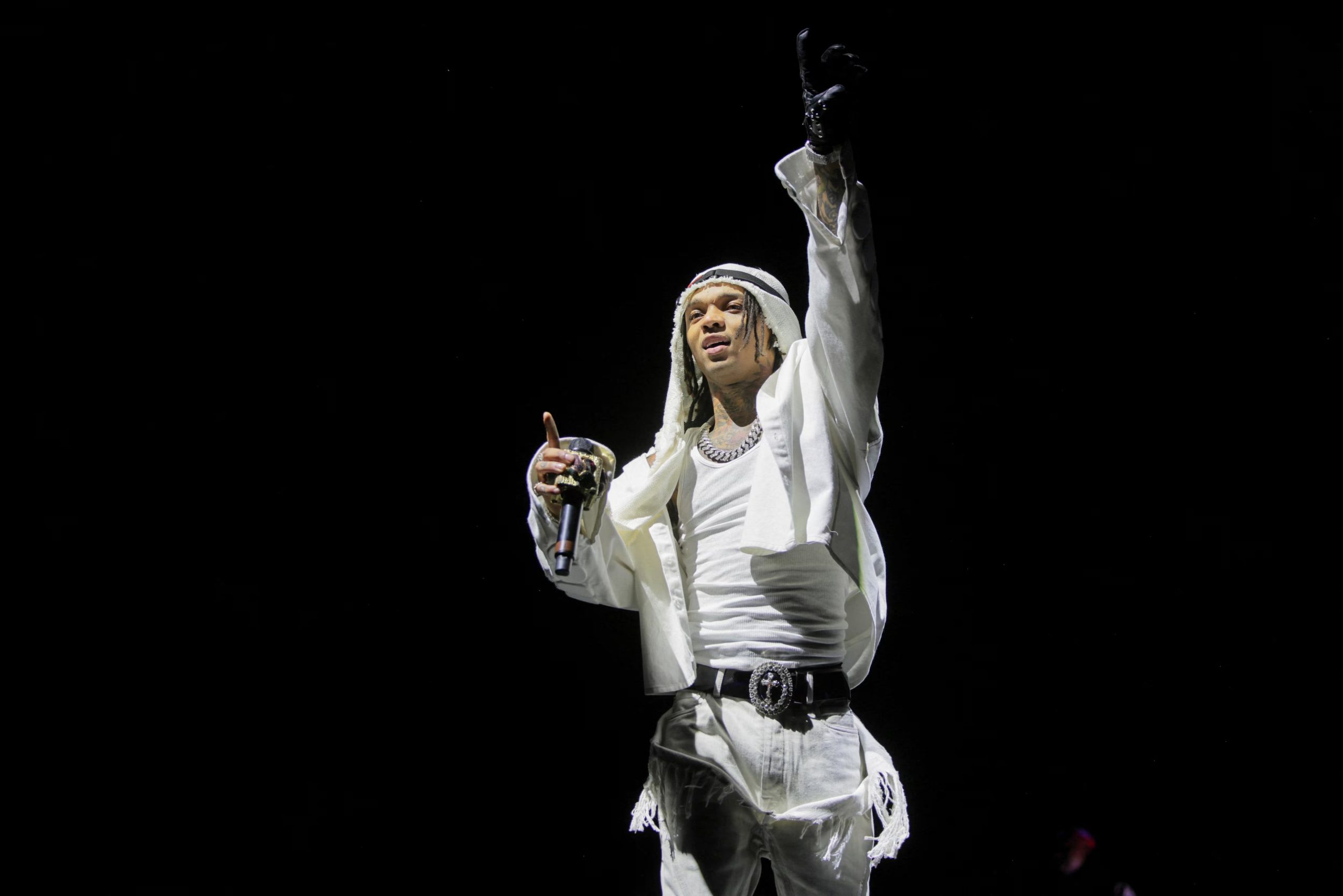 Swae Lee destacó en el escenario con un conjunto blanco de campera abierta, pantalones con flecos, cinturón decorativo, guantes oscuros y cadenas plateadas, imponiendo estilo propio entre los asistentes (REUTERS/Daniel Cole)