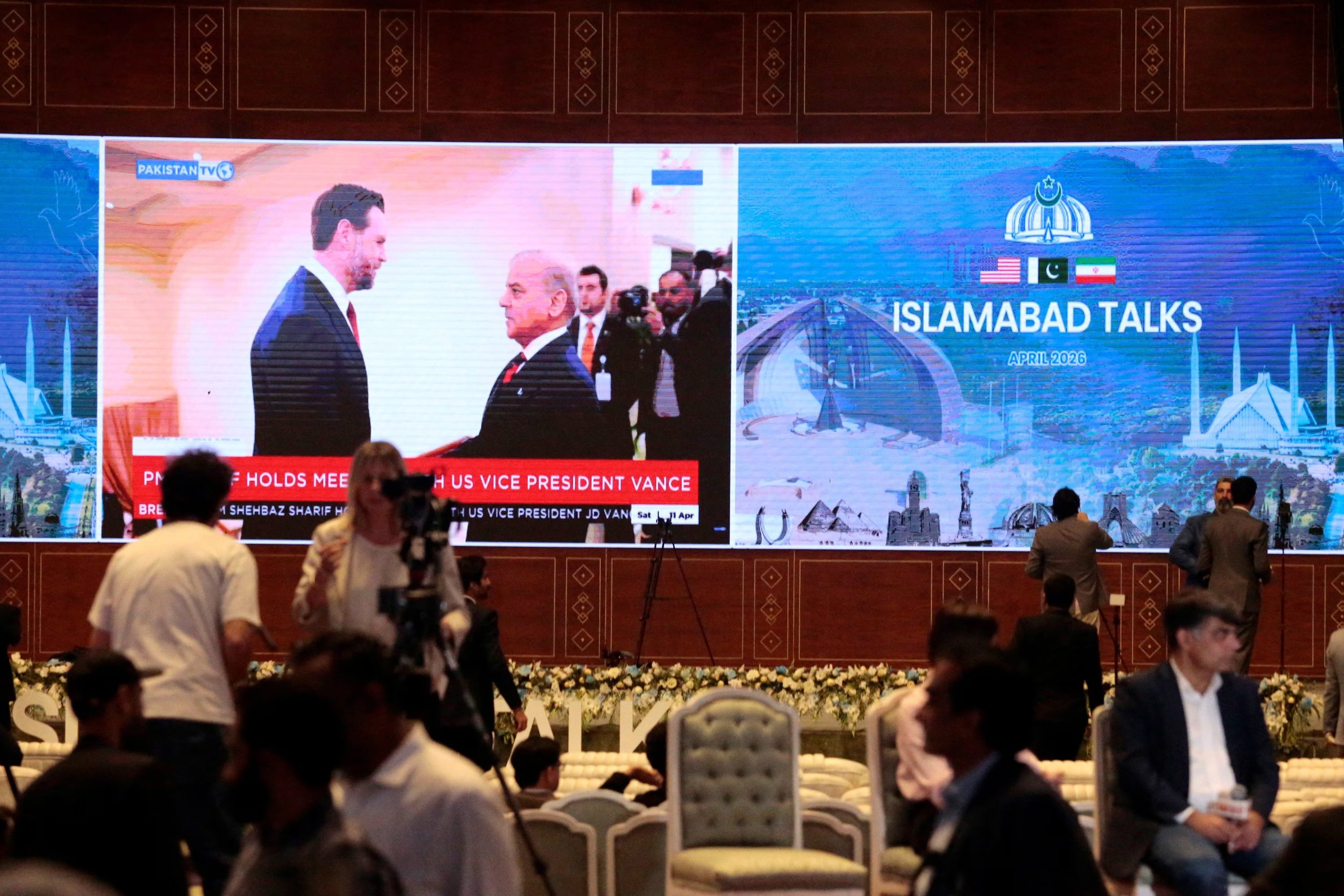 Periodistas trabajan mientras una pantalla muestra noticias con una imagen del primer ministro de Pakistán, Shehbaz Sharif, reunido con el vicepresidente de EEUU, JD Vance, en un centro de prensa instalado para la cobertura de las conversaciones de paz entre EEUU e Irán en Islamabad, Pakistán, 11 de abril de 2026 (REUTERS/Asim Hafeez)