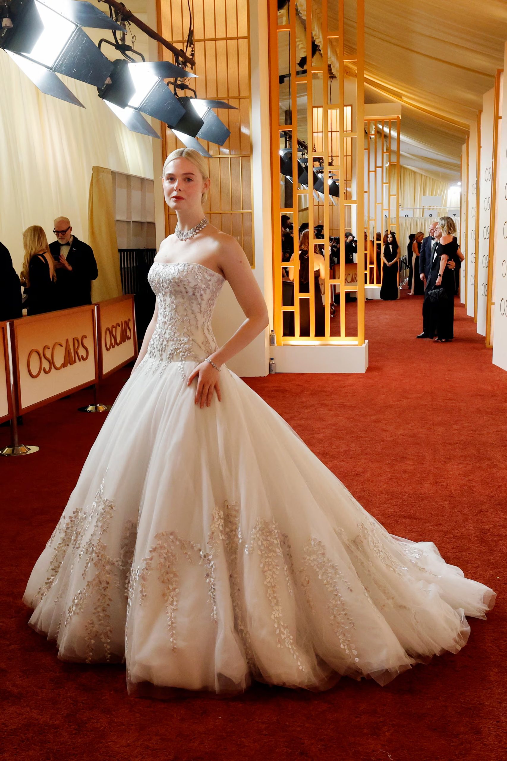 Los bordados y apliques metálicos en el vestido blanco de gala de Elle Fanning aportan brillo y movimiento, realzando el corte princesa y ofreciendo un aire festivo con cada paso en eventos especiales (REUTERS/Carlos Barria)