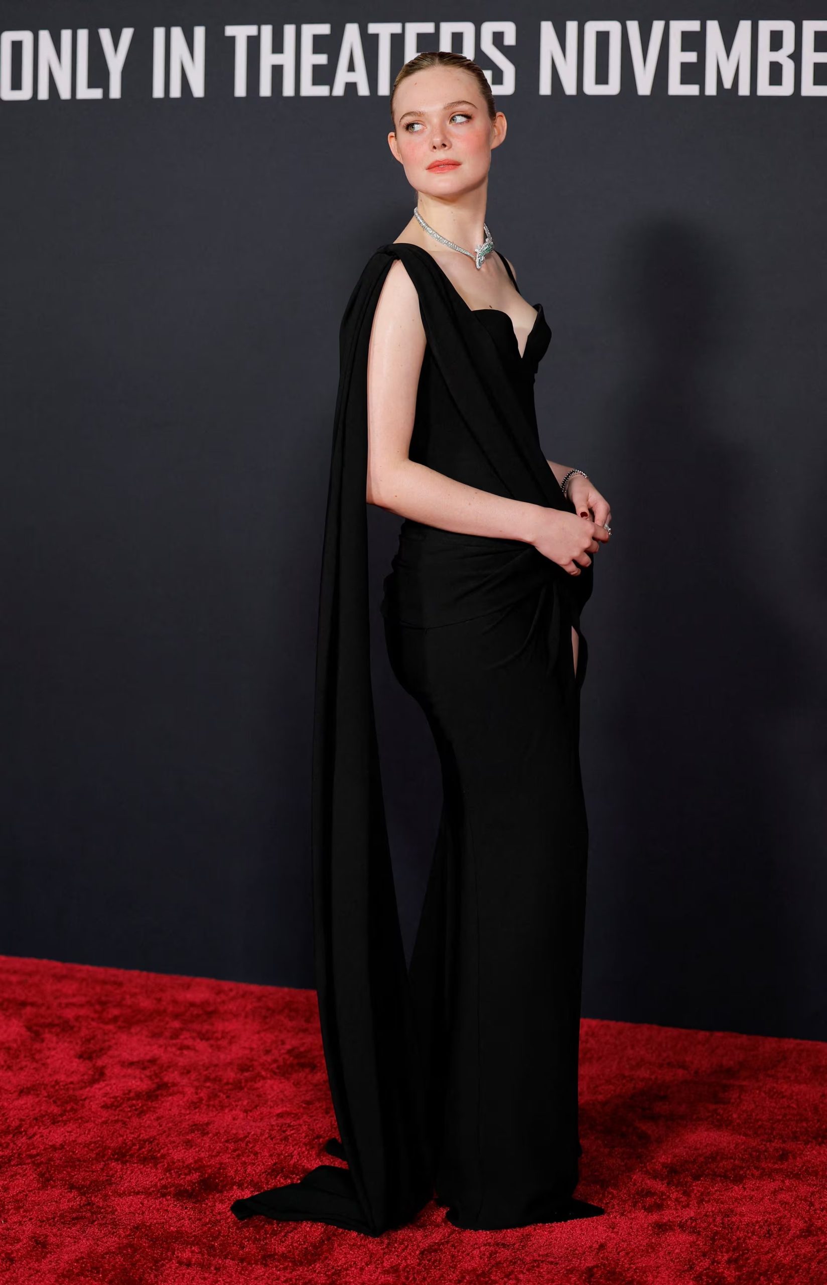  La capa y el escote corazón renuevan el vestido negro de Elle Fanning, añadiendo dinamismo y volumen a un conjunto que combina líneas ajustadas y accesorios plateados en una propuesta moderna La combinación de prendas firmadas por August Barron muestra la disposición de Elle Fanning para explorar nuevas vías de expresión a través de la moda, consolidando su versatilidad y audacia estilística (REUTERS/Mike Blake)