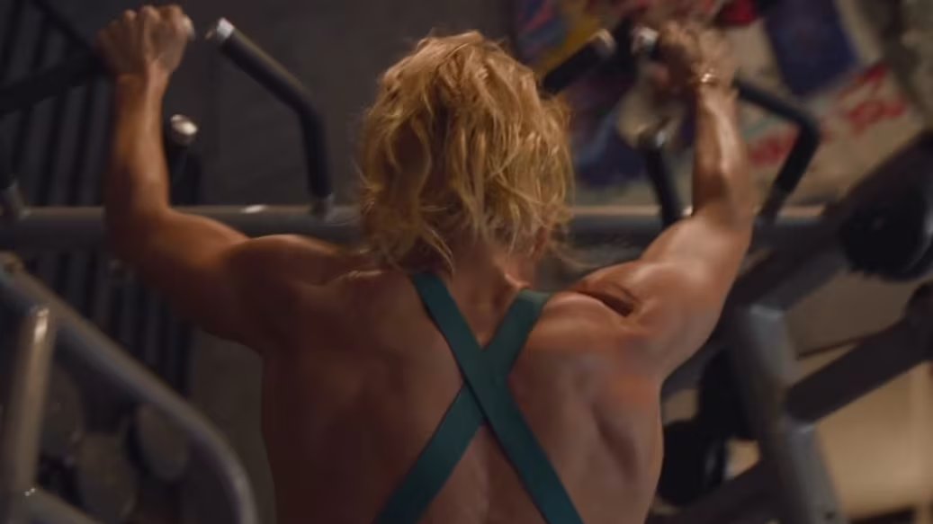 Una persona musculosa con cabello rubio realiza un ejercicio de fuerza en el gimnasio, mostrando su dedicación al entrenamiento físico.