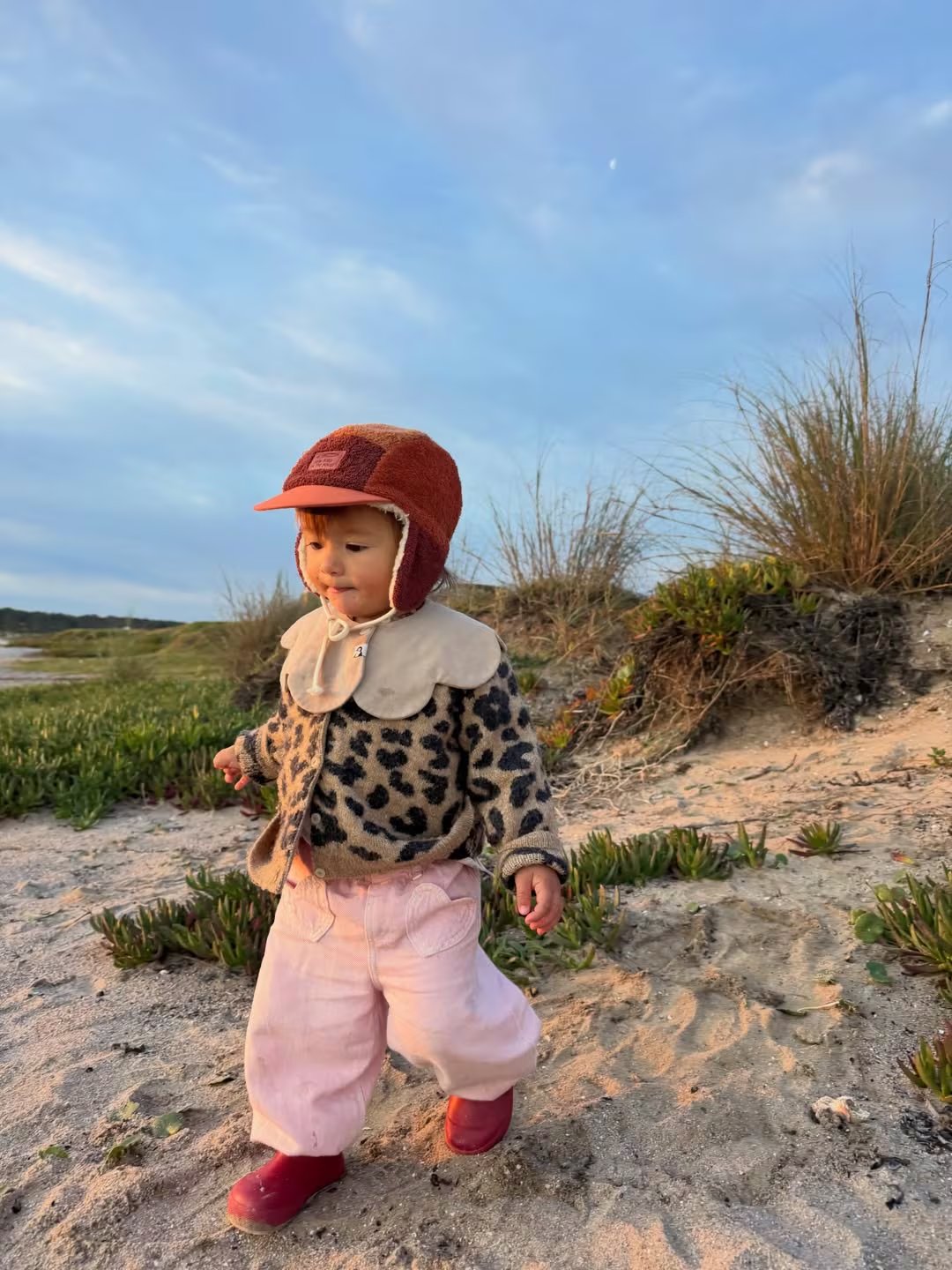 La hija de Calu explora el campo en Uruguay, disfrutando de un hermoso atardecer entre la arena y la vegetación costera