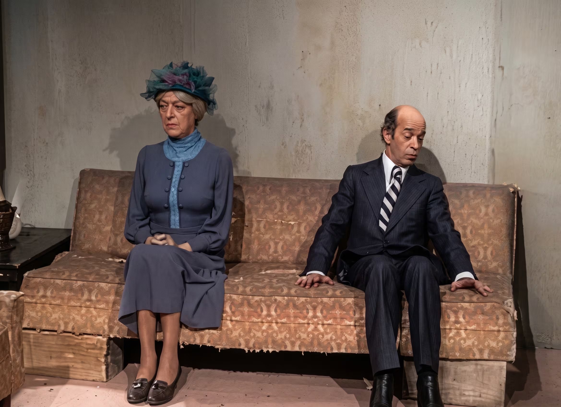 El reconocido actor Ricardo Pascual, parte de El Chavo del 8 en los años 70, se presenta en una escena teatral junto a una actriz, ambos sentados en un sofá vintage. (Captura de pantalla: YouTube)