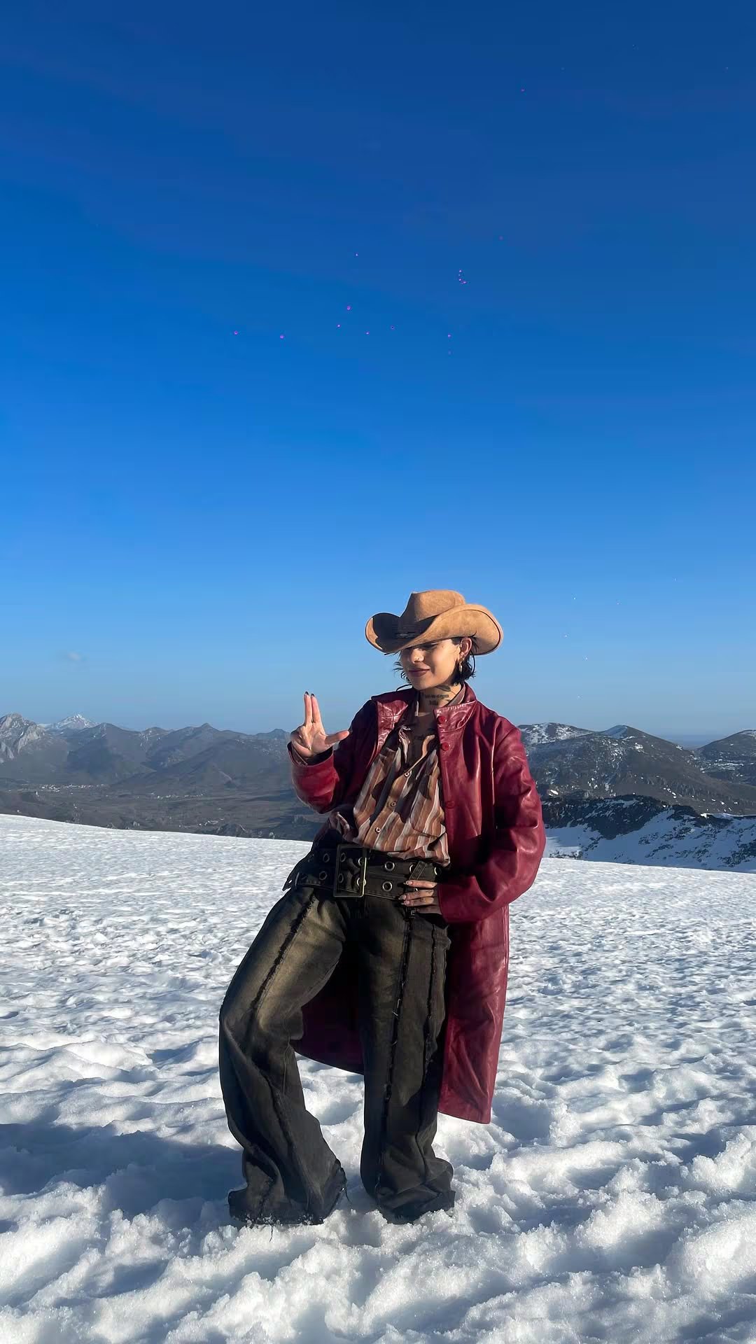 Dagna Mata, modelo del videoclip 'Un vals' de Christian Nodal, posa en un paisaje nevado con un distintivo atuendo vaquero bajo un cielo azul claro. (Dagna Mata: Instagram)