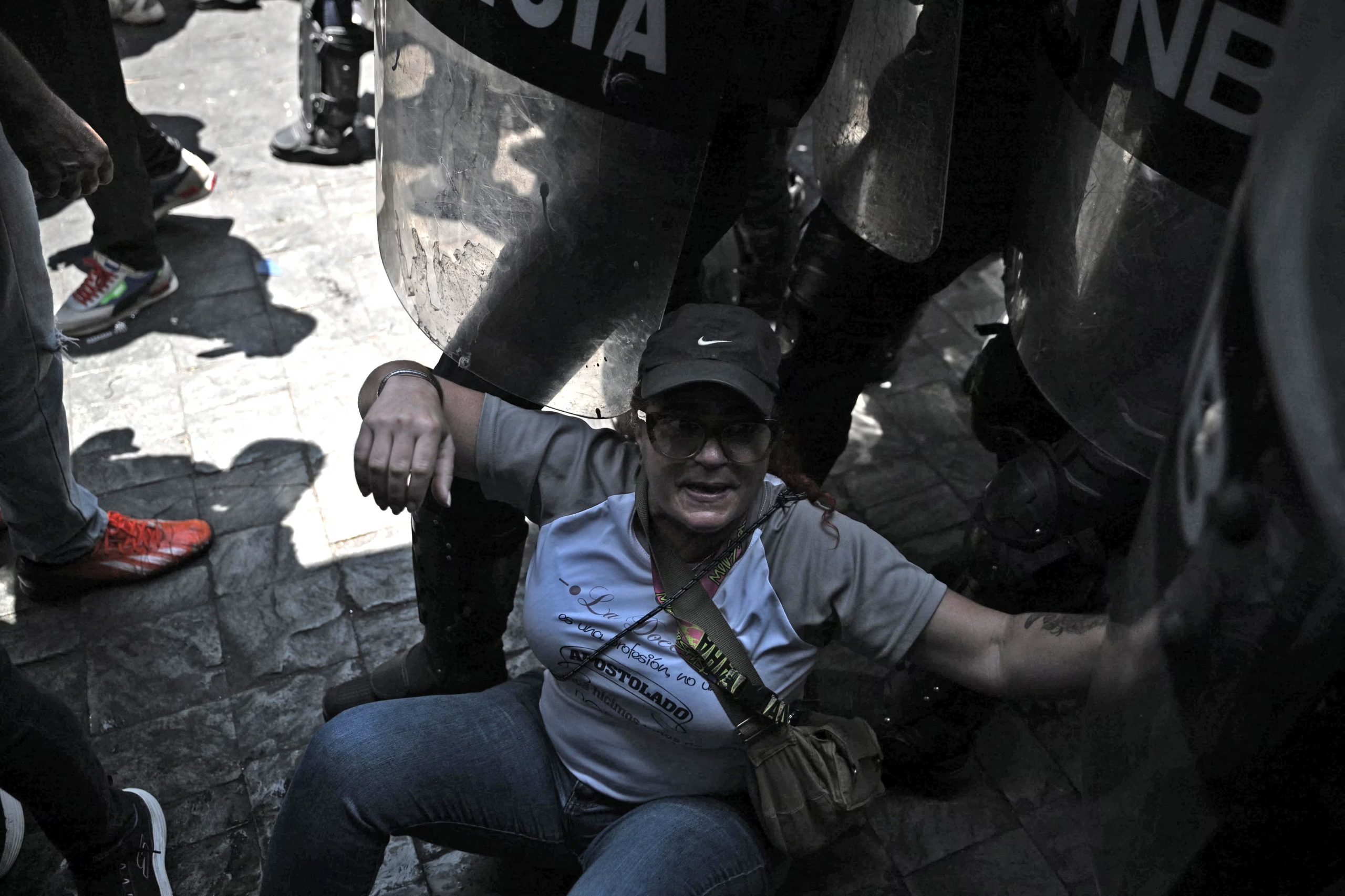 Una mujer es empujada contra el suelo mientras se encuentra rodeada por policías (AFP)