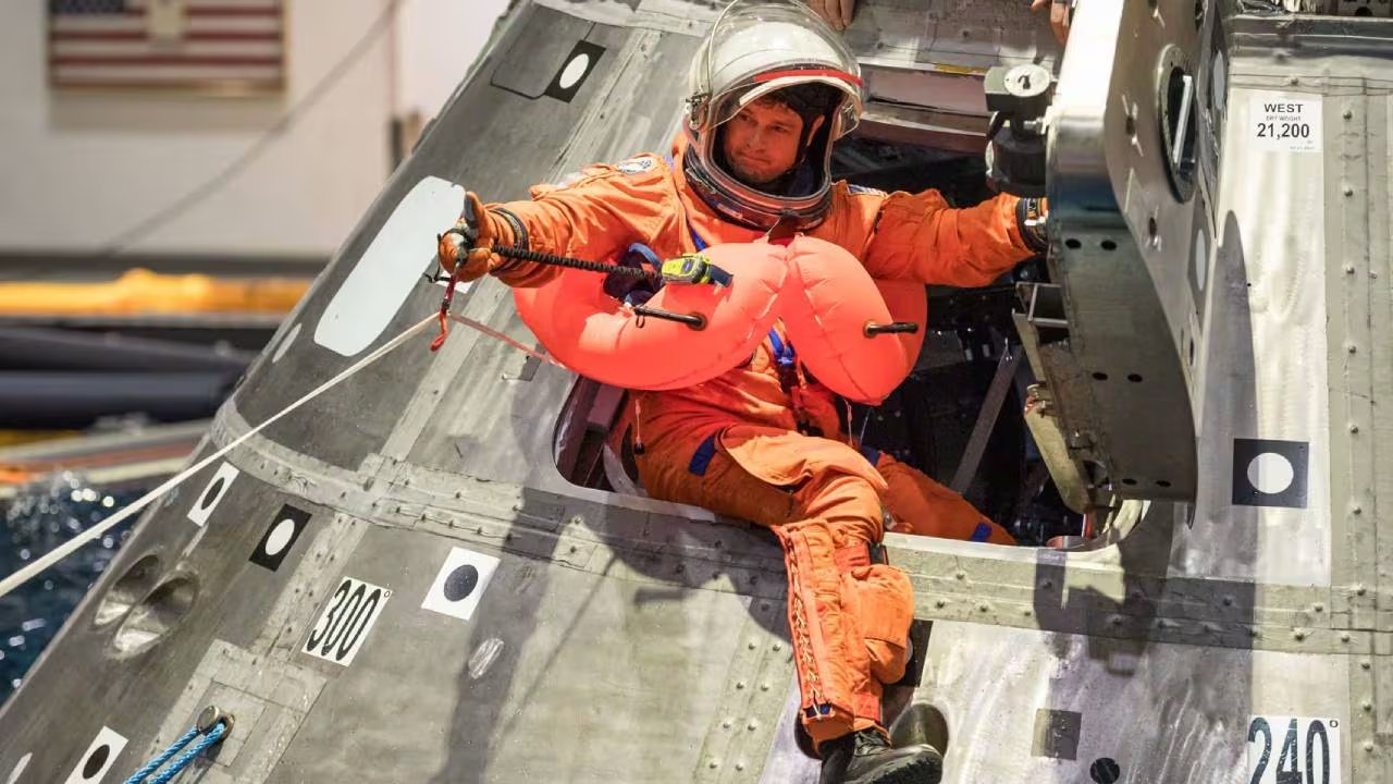 Un miembro de la tripulación con traje de vuelo y chaleco salvavidas inflado emerge de una cápsula espacial durante un ejercicio de recuperación acuática. (NASA)