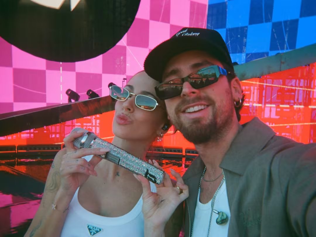 Tini Stoessel posa con un micrófono brillante junto a un hombre sonriente en el vibrante escenario de su concierto en Rosario.