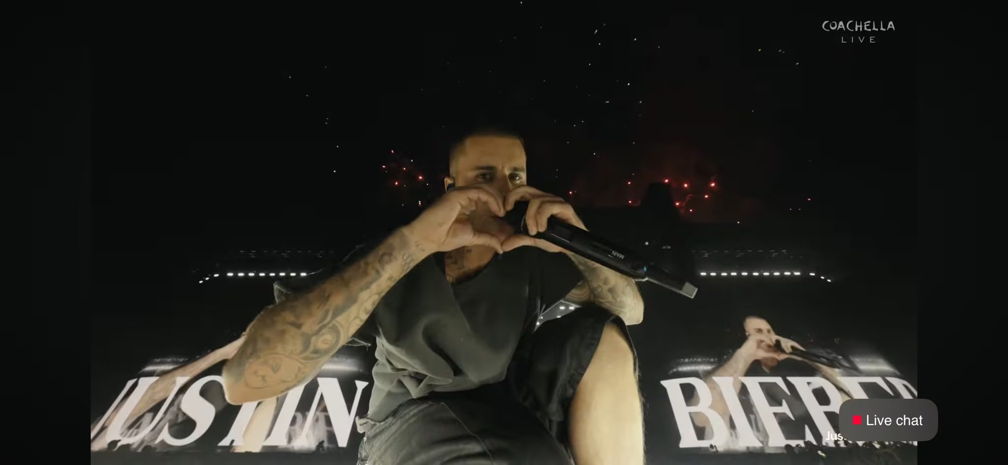 Justin Bieber saluda al público en Coachella 2026 formando un corazón con las manos mientras sostiene un micrófono durante su actuación en vivo. (Coachella)