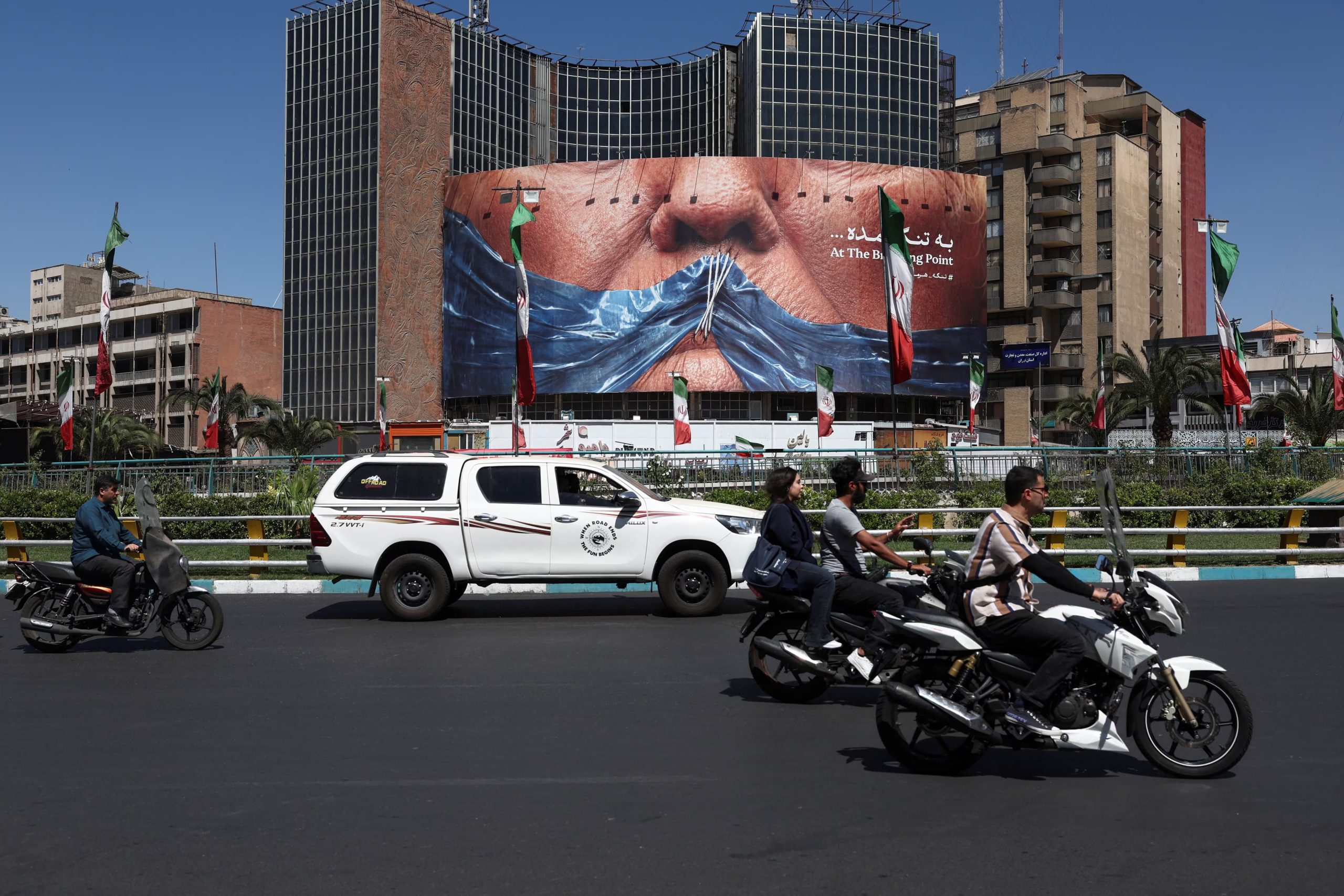 Varias personas pasan en bicicleta junto a una valla publicitaria antiestadounidense que representa al presidente de Estados Unidos, Donald Trump, y el estrecho de Ormuz, en Teherán, Irán, el 25 de mayo de 2026 (Majid Asgaripour/WANA vía REUTERS)
