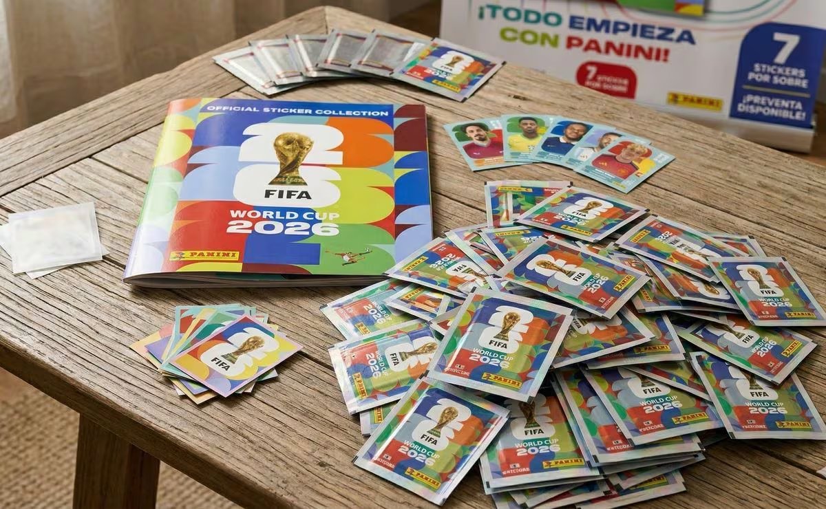 El álbum oficial de figuritas Panini FIFA World Cup 2026, junto con numerosos sobres y figuritas sueltas, se exhiben en una mesa de madera, listos para coleccionistas. (Redes sociales)
